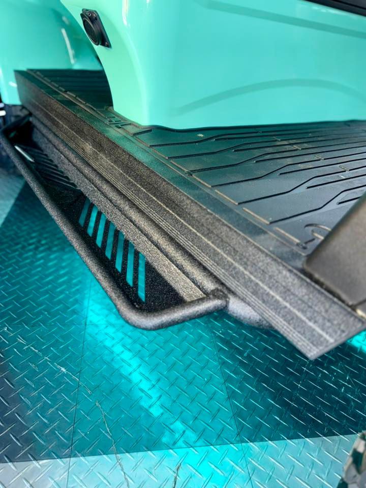 Black running board on a teal-colored vehicle, angled view. Textured black mat in bed.