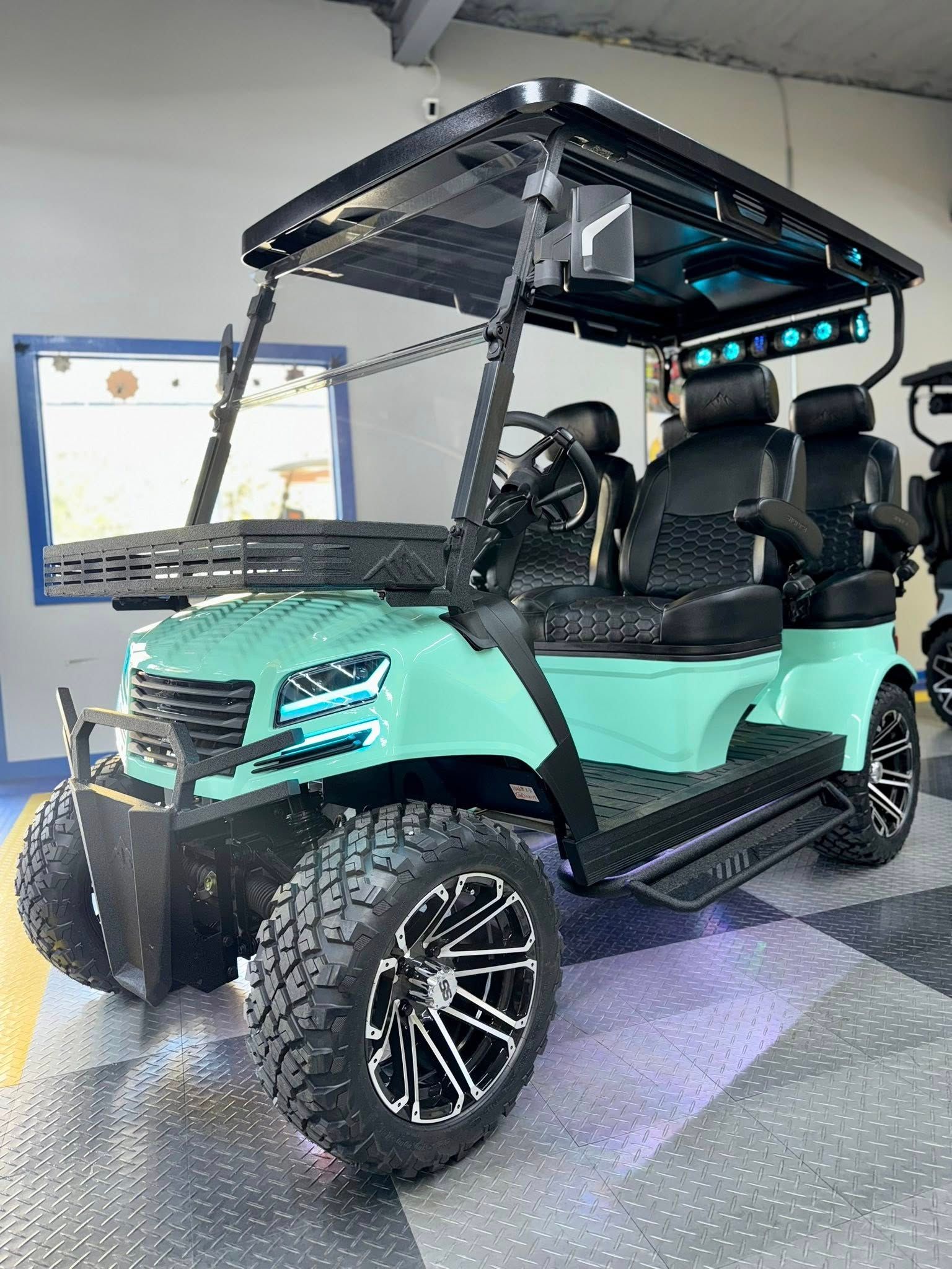 Teal customized golf cart with black accents, large tires, and LED lights. Indoors.