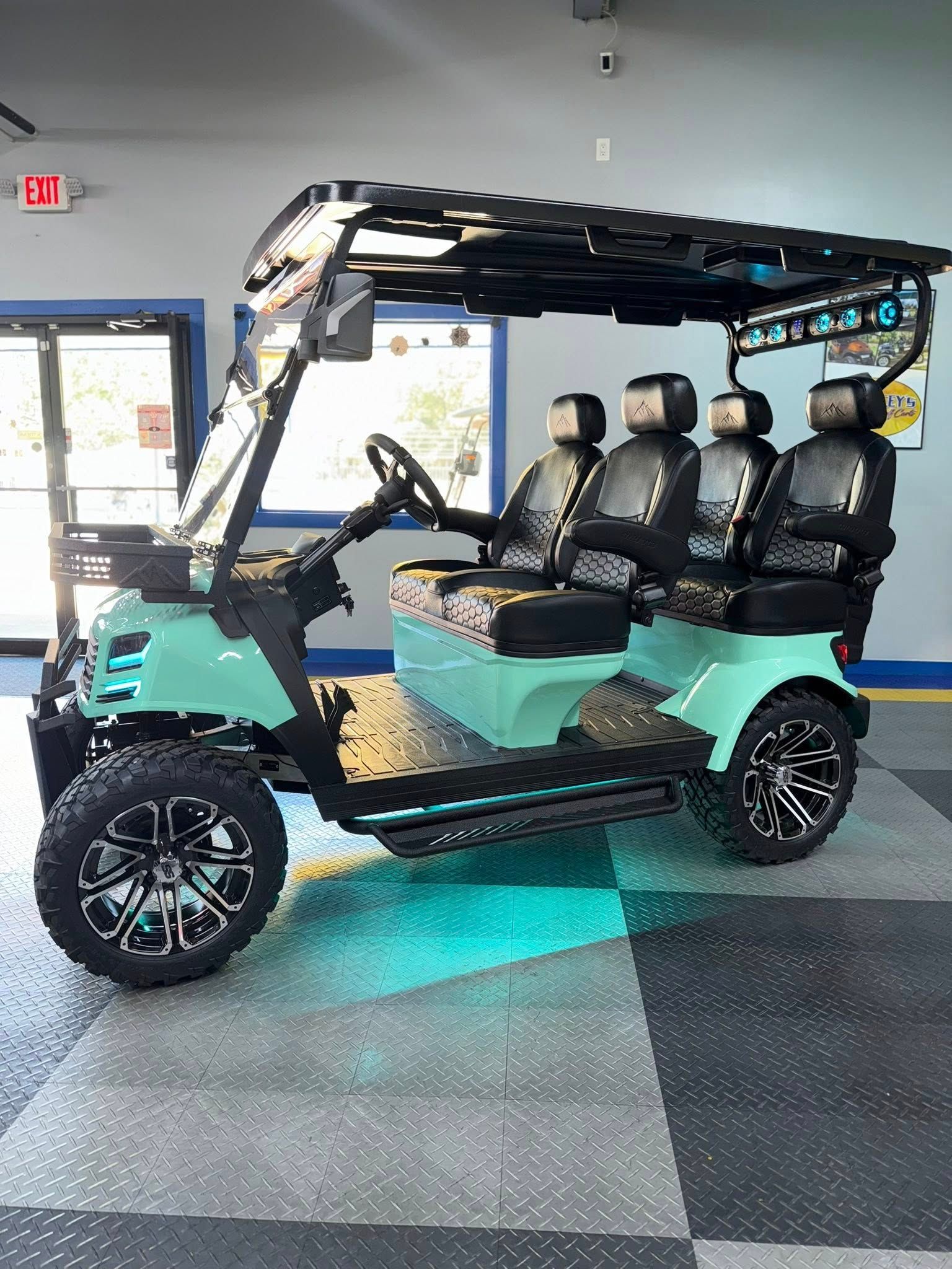 Teal golf cart with black accents, seating four, on a tiled floor.
