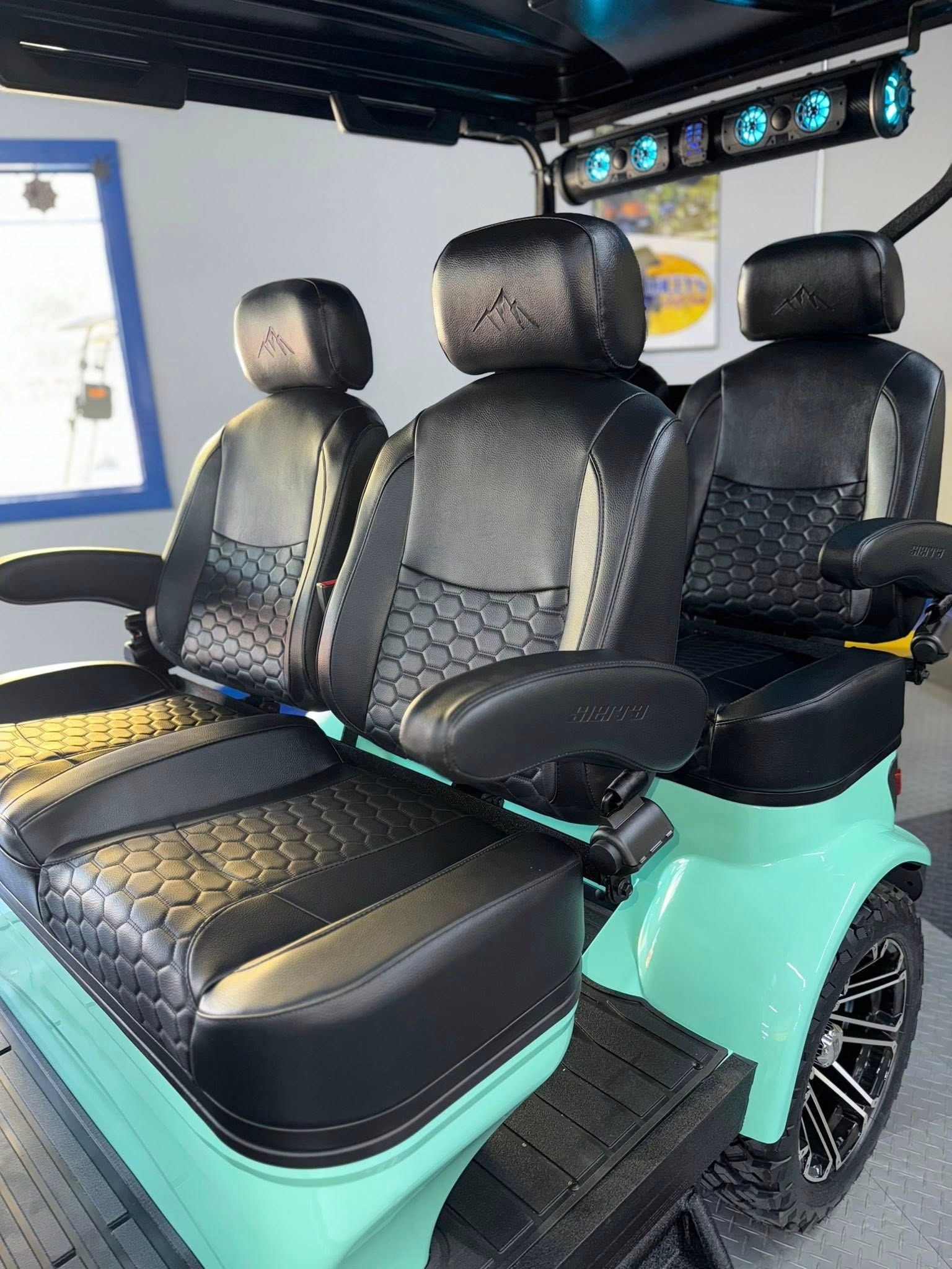 A custom teal golf cart with black seats and trim, a blue light bar, and black wheels.