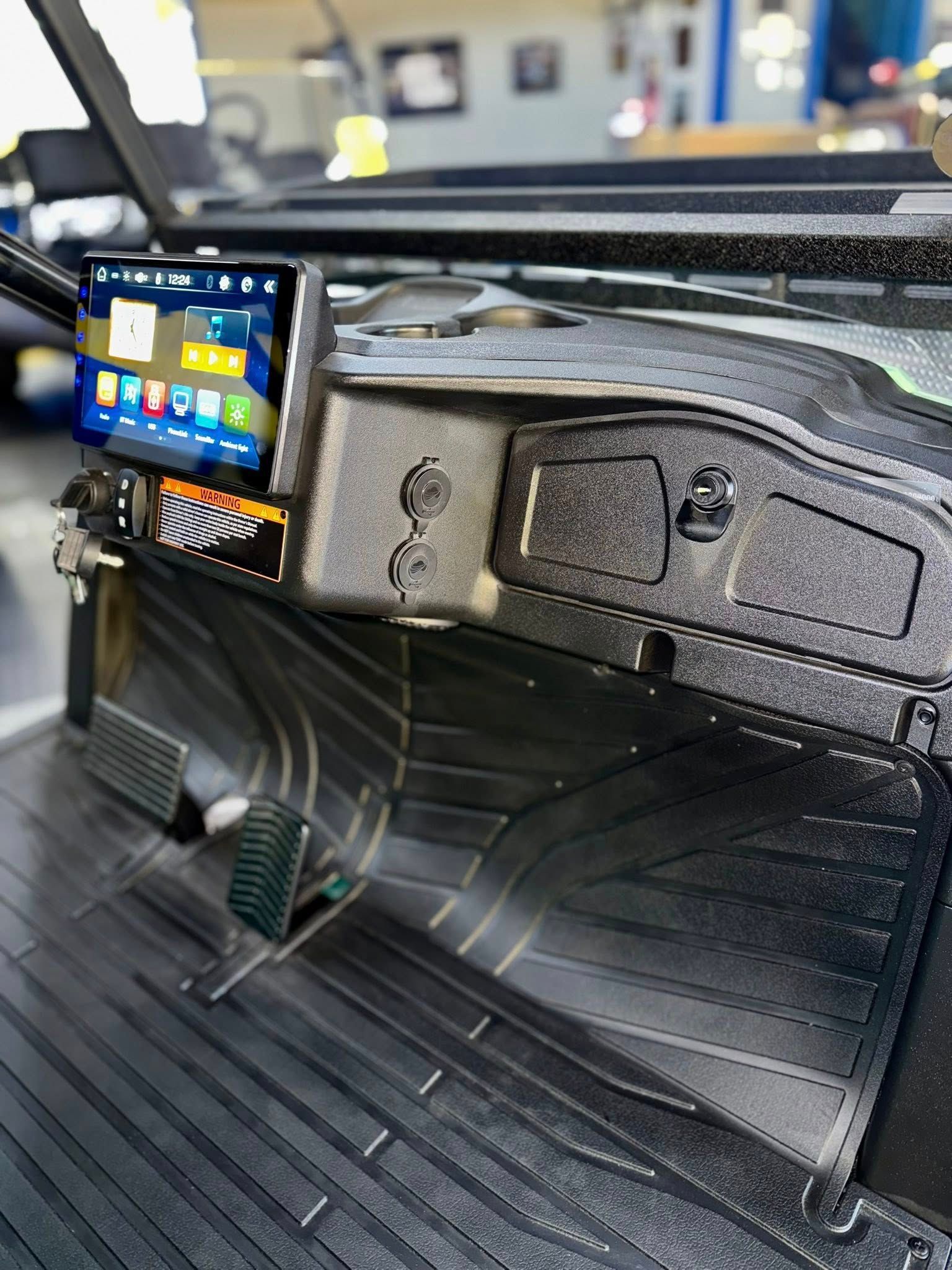 Black dashboard with touchscreen, switches, pedals, and floor mat.