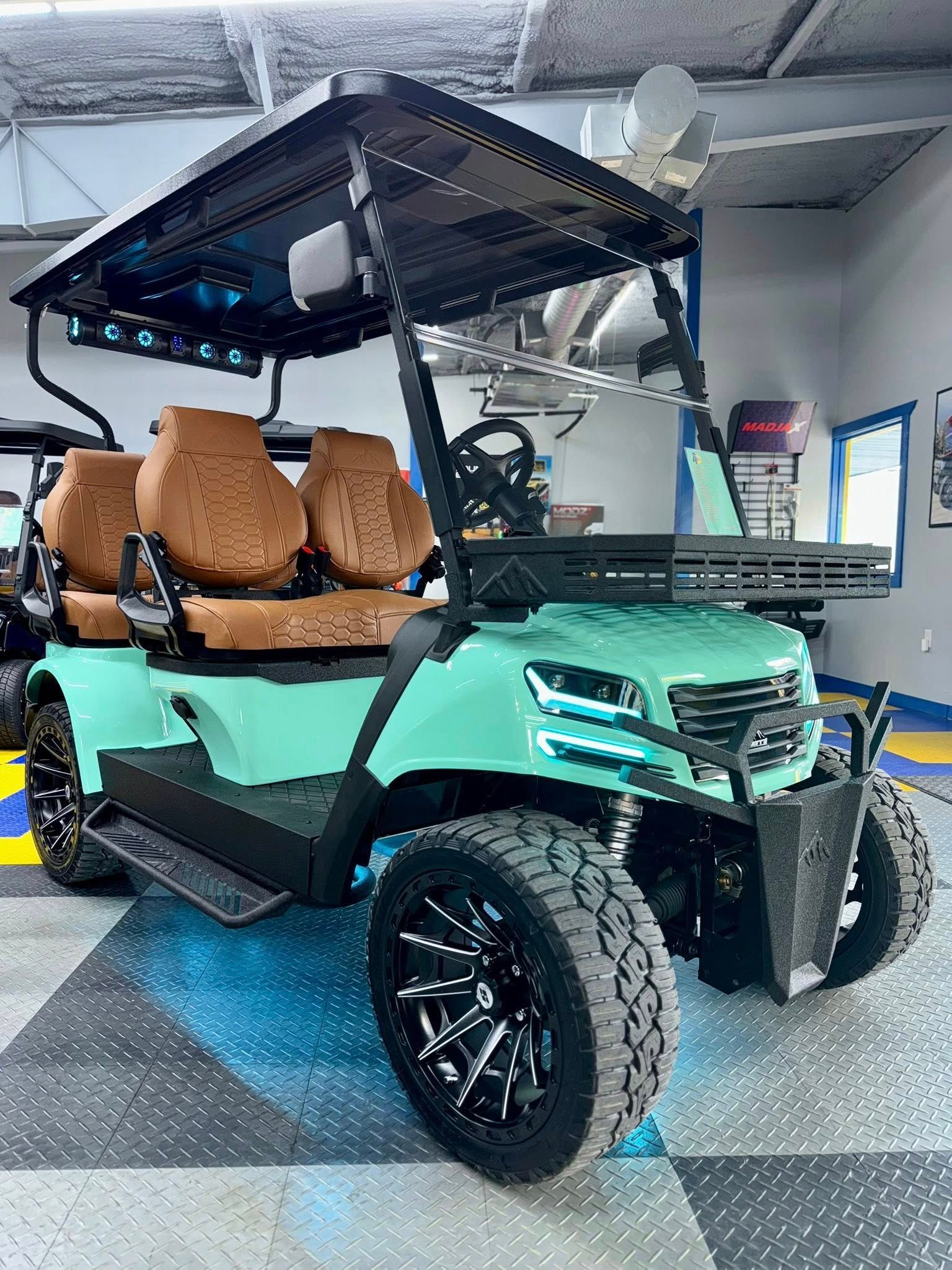 Mint green golf cart with brown seats, black wheels, and a black roof, parked indoors.