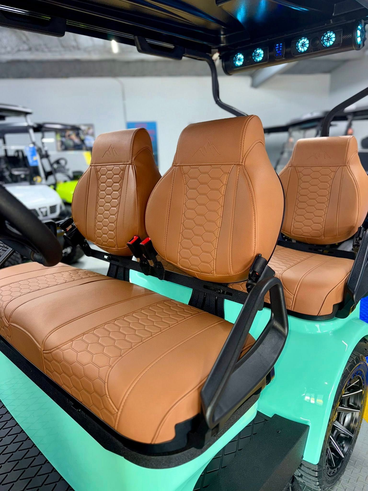 Brown and teal golf cart seats with a black armrest, parked inside a garage.