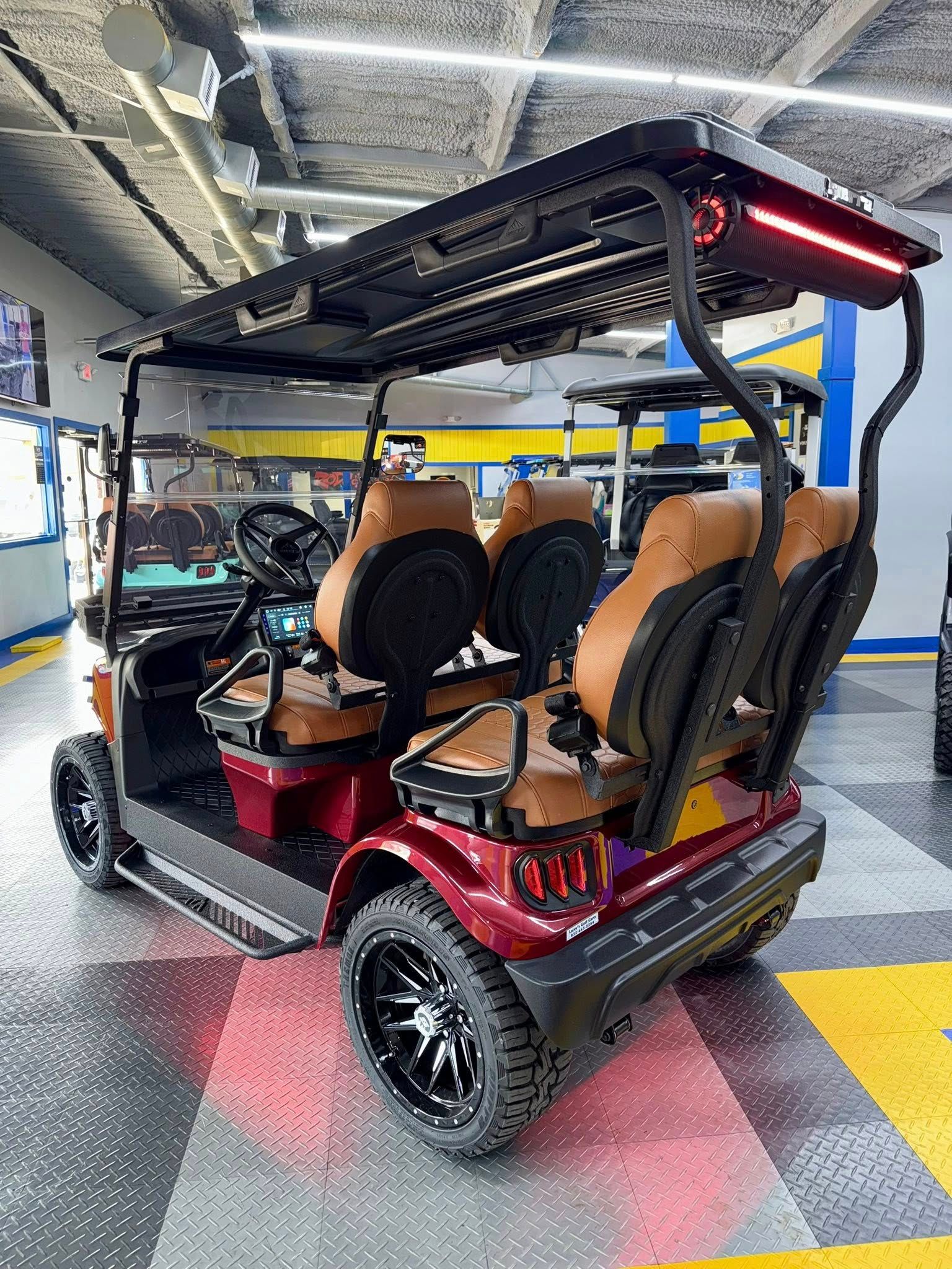 Burgundy golf cart with brown seats, black roof, and custom wheels in a showroom.