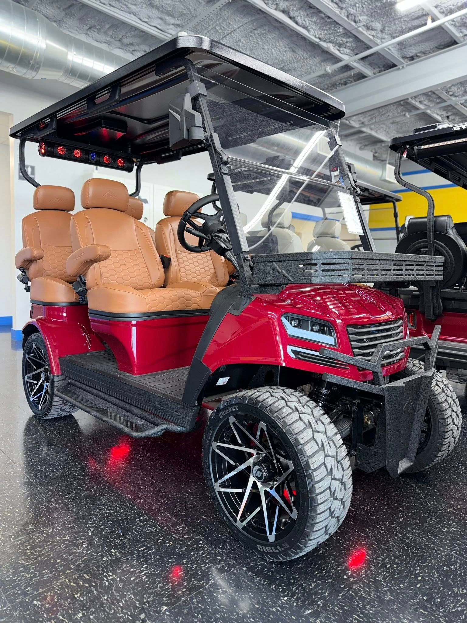 Red and black golf cart with tan seating, custom wheels, and rugged tires, parked indoors.