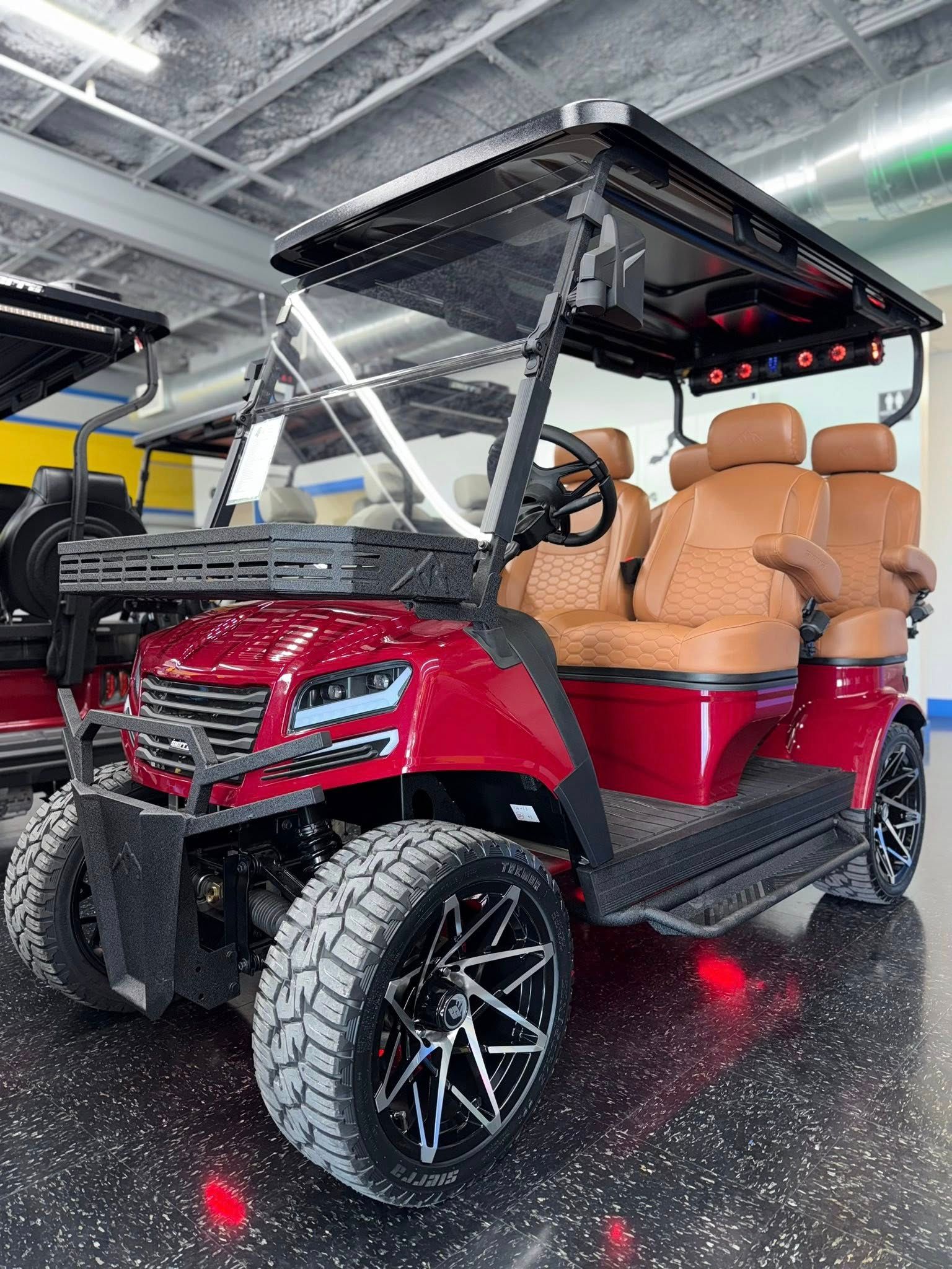 Red golf cart with brown seating, black wheels, and a black roof, indoors.