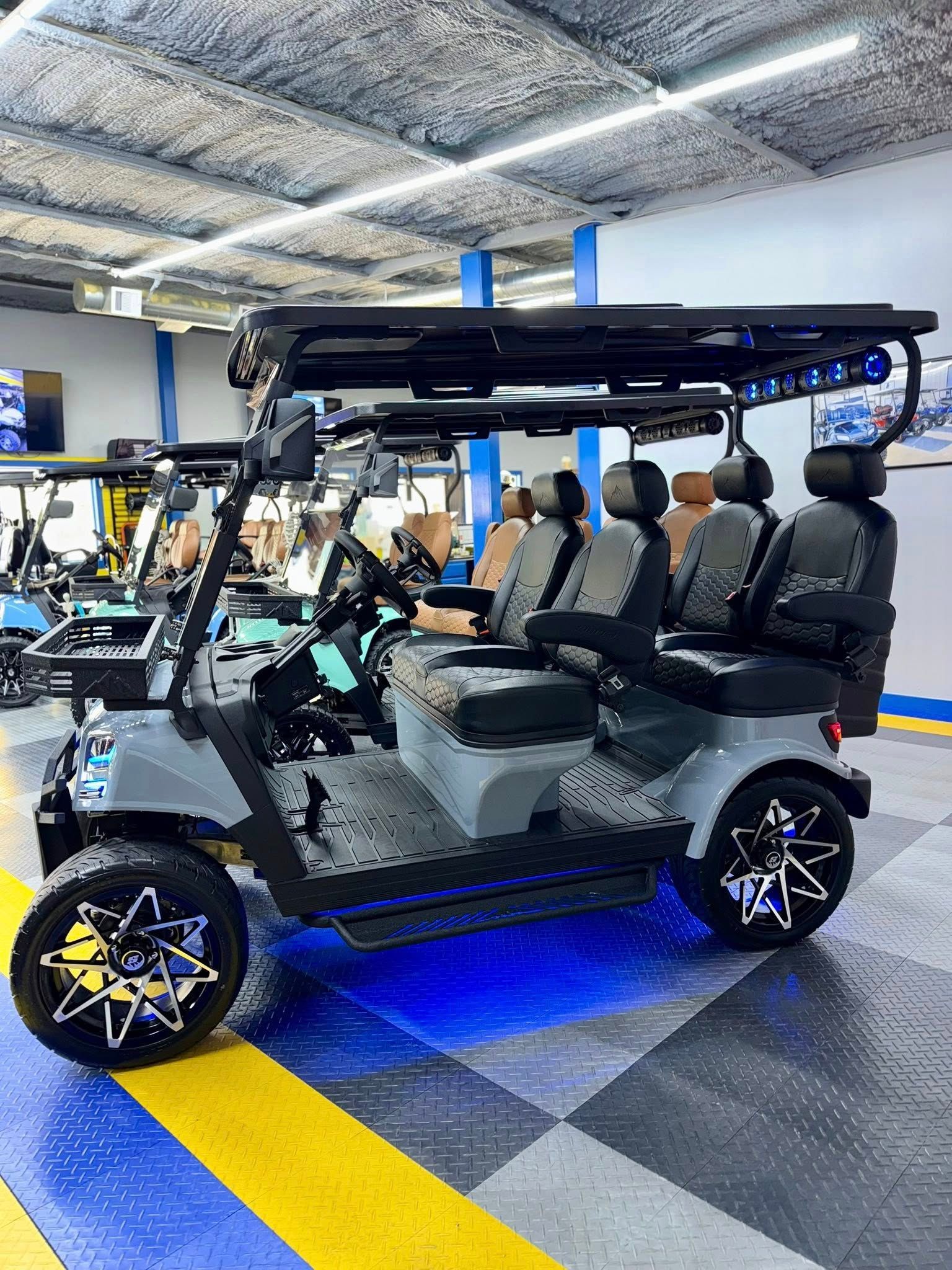 Grey customized golf cart with blue underglow, black rims, and a roof rack in a showroom.