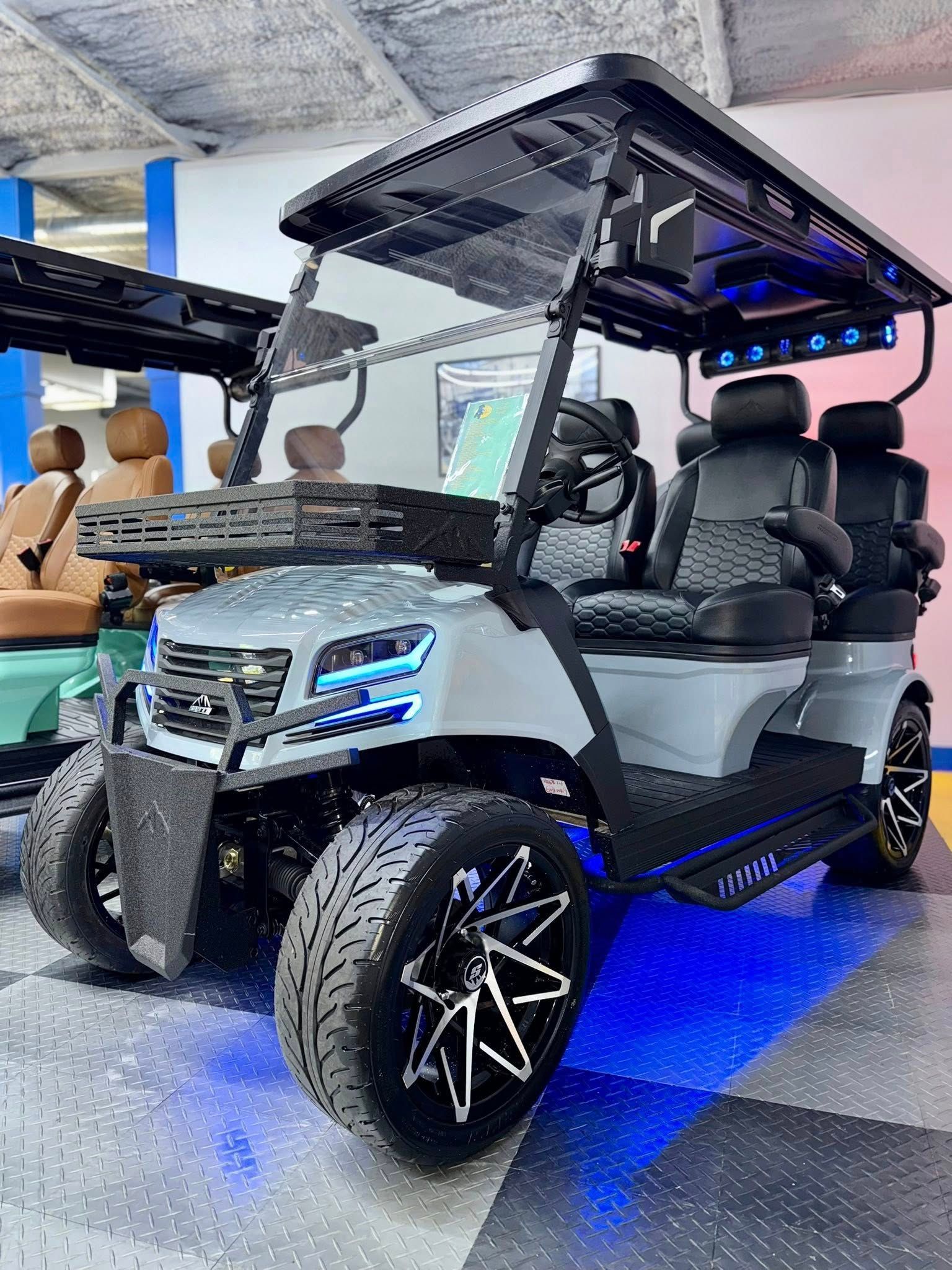Gray and black golf cart with blue LED lights, large tires, and custom seating indoors.