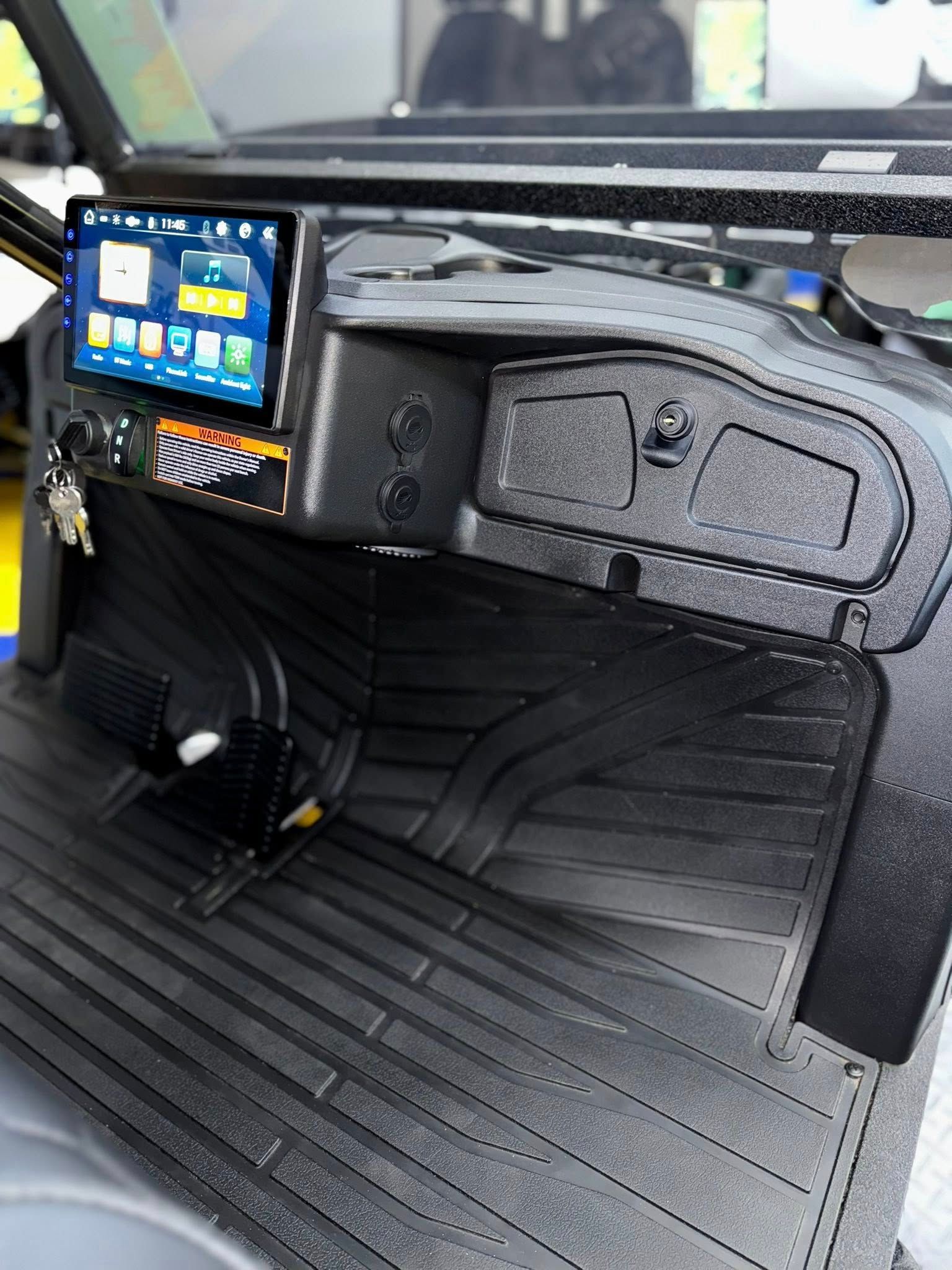 Black golf cart dashboard with a touchscreen, switches, rubber floor, and storage compartments.