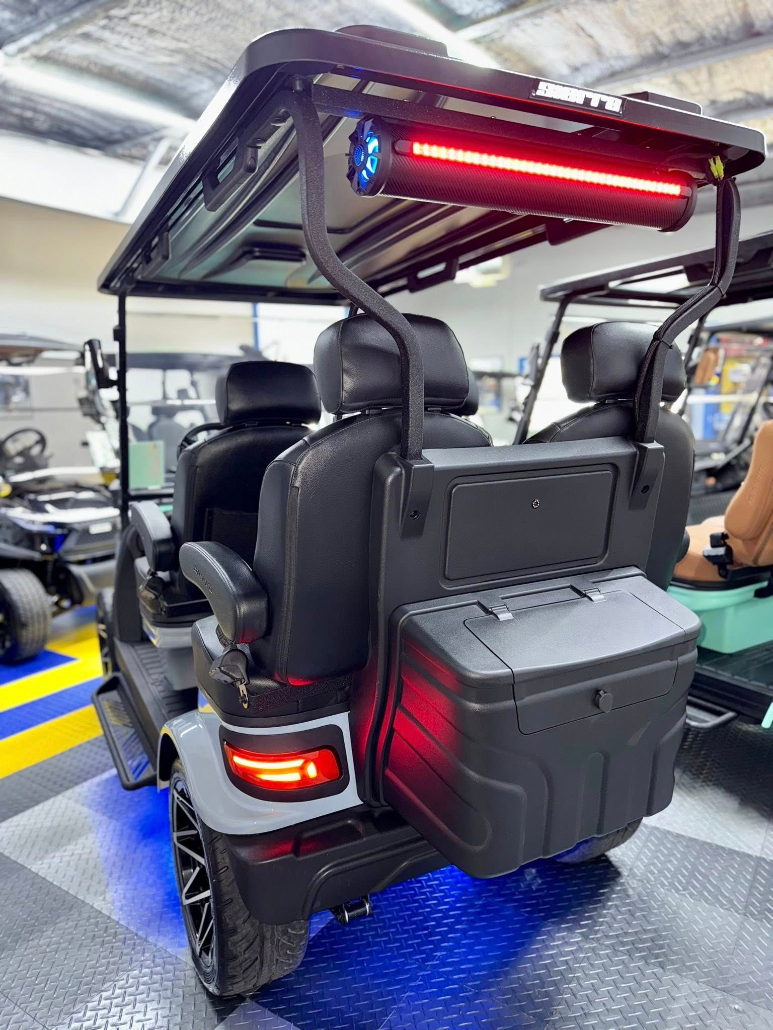 Grey golf cart with black seats, LED lights, and storage box in a garage setting.