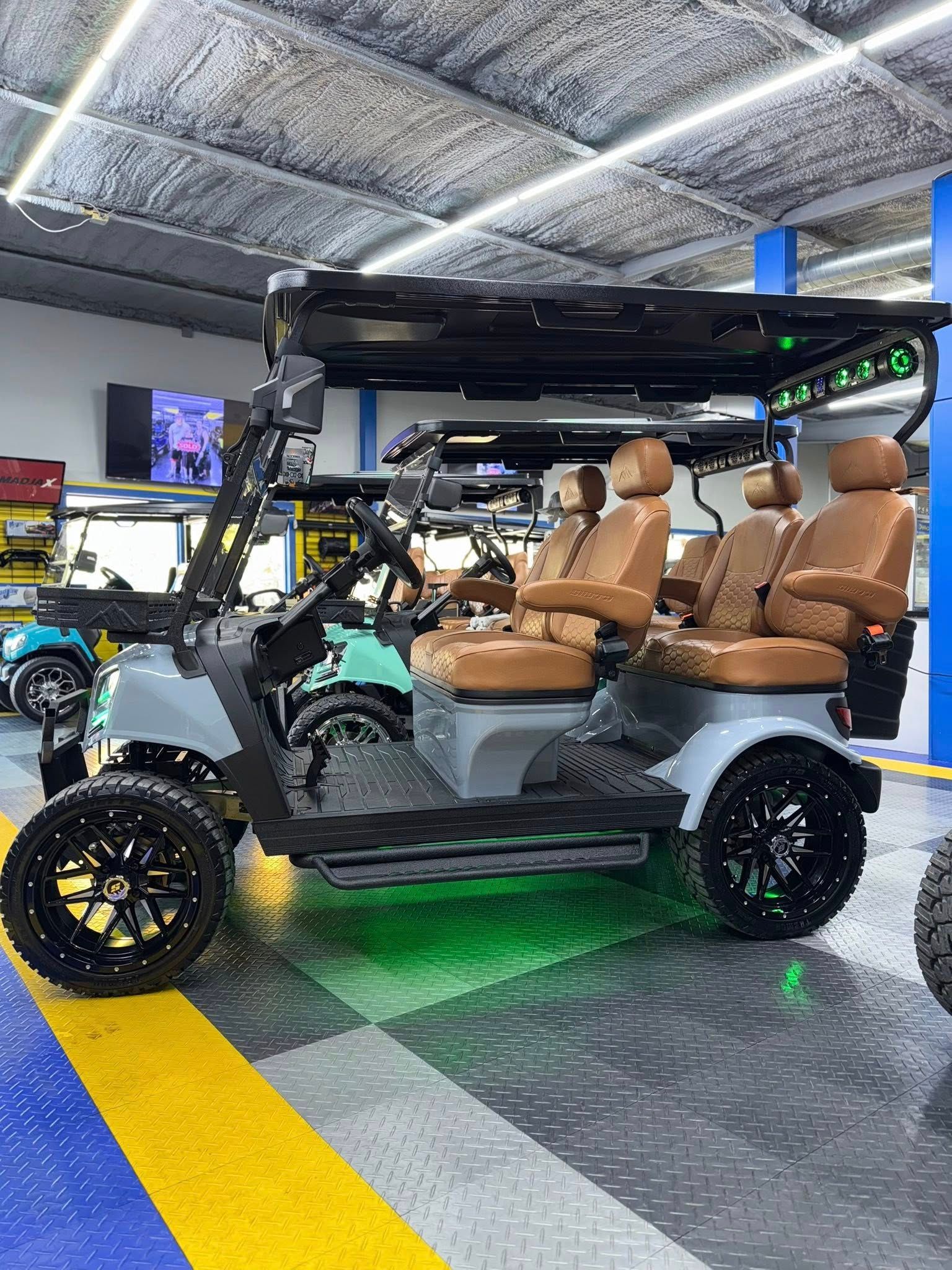 Gray golf cart with brown seats, black wheels and roof rack, neon green underglow in a showroom.