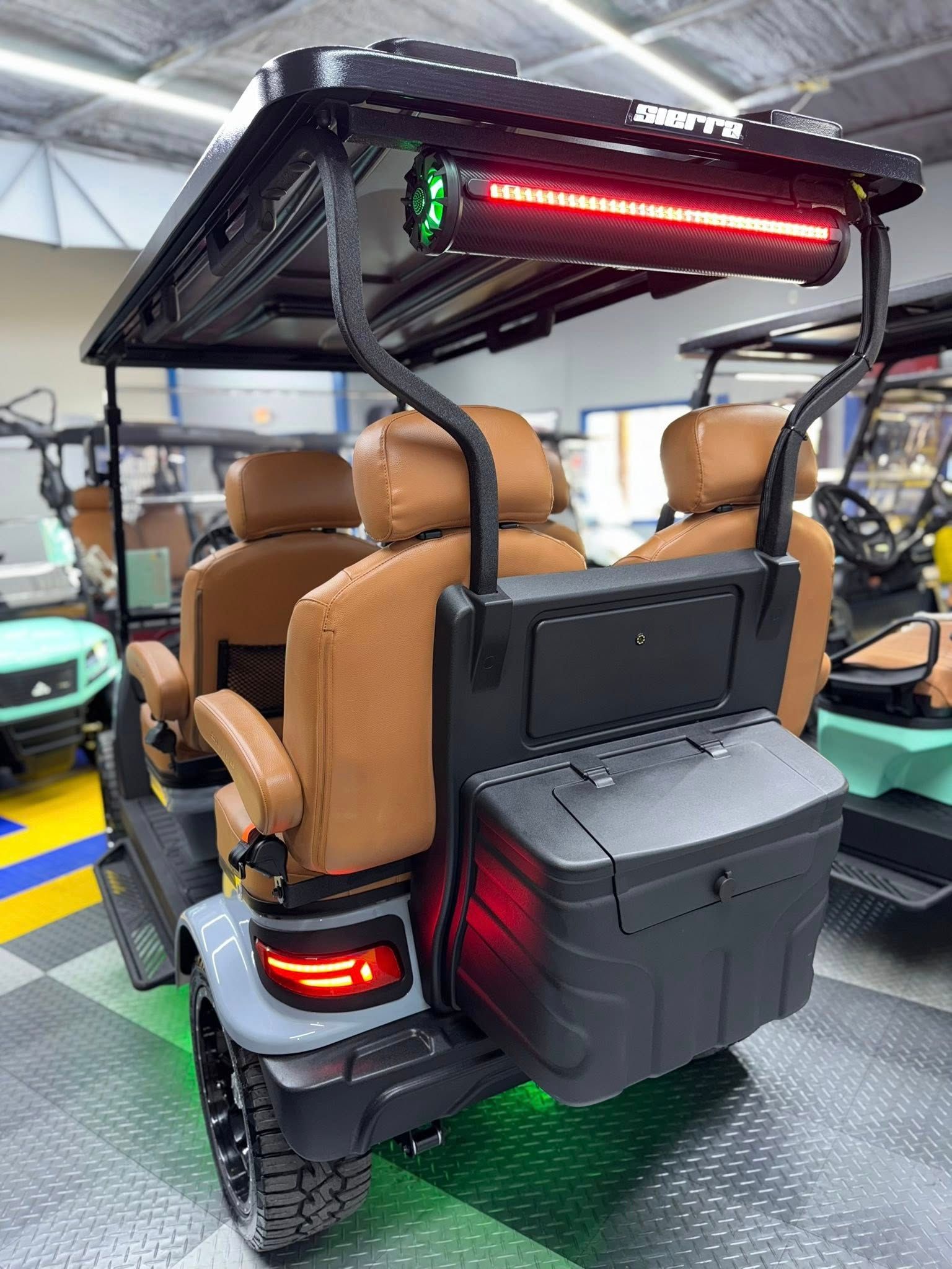 Gray golf cart with tan seats, black roof, and storage box. Red LED light bar is mounted.
