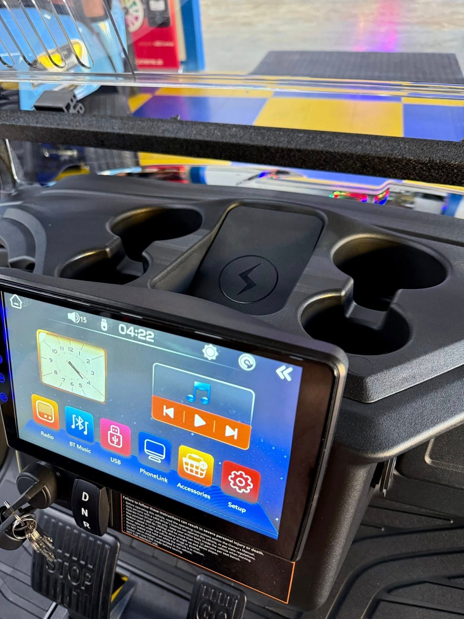 Dashboard of a golf cart with a digital display, wireless charger, and cup holders.