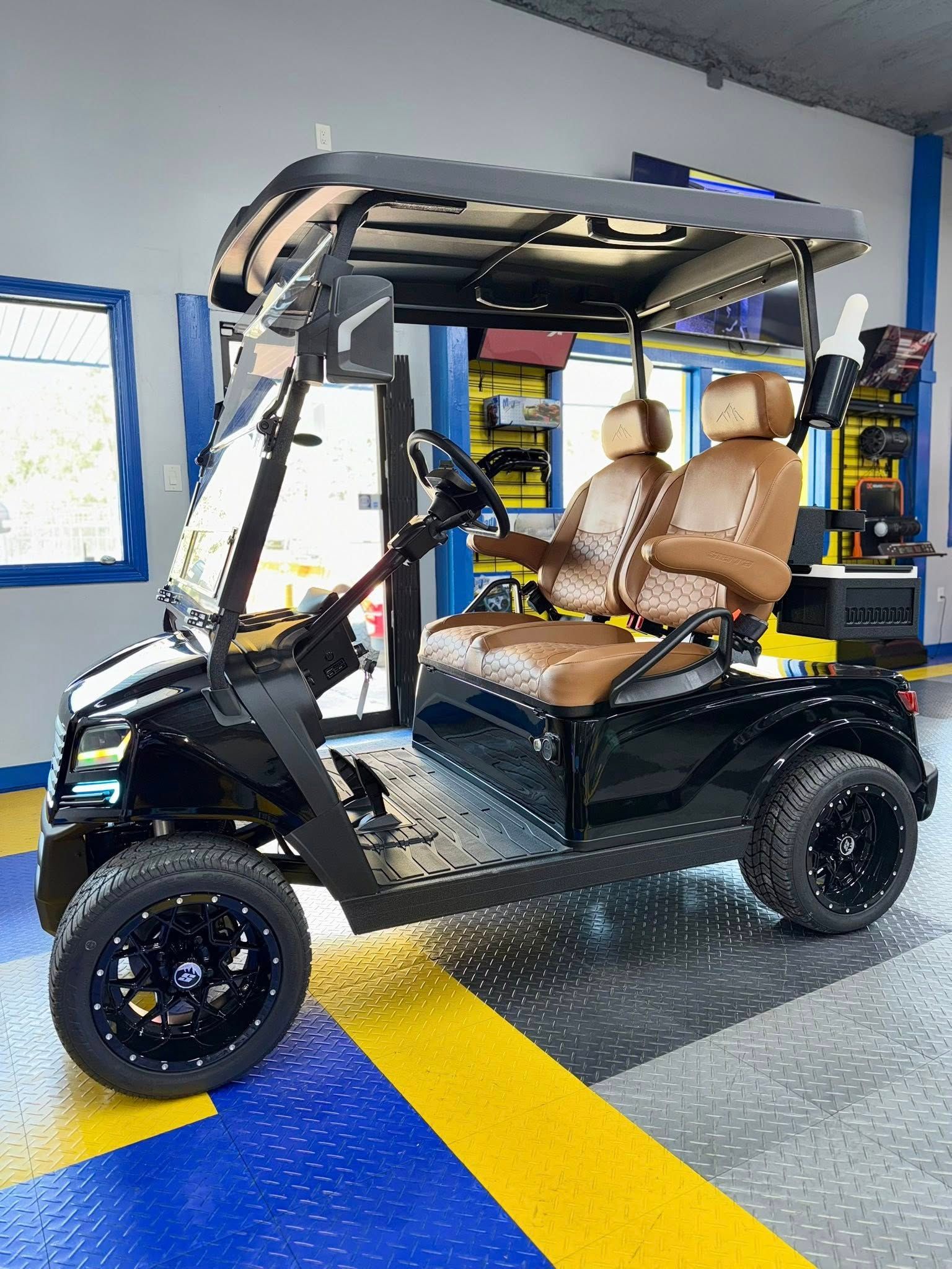 Black golf cart with tan seats, black wheels, and a canopy, indoors.