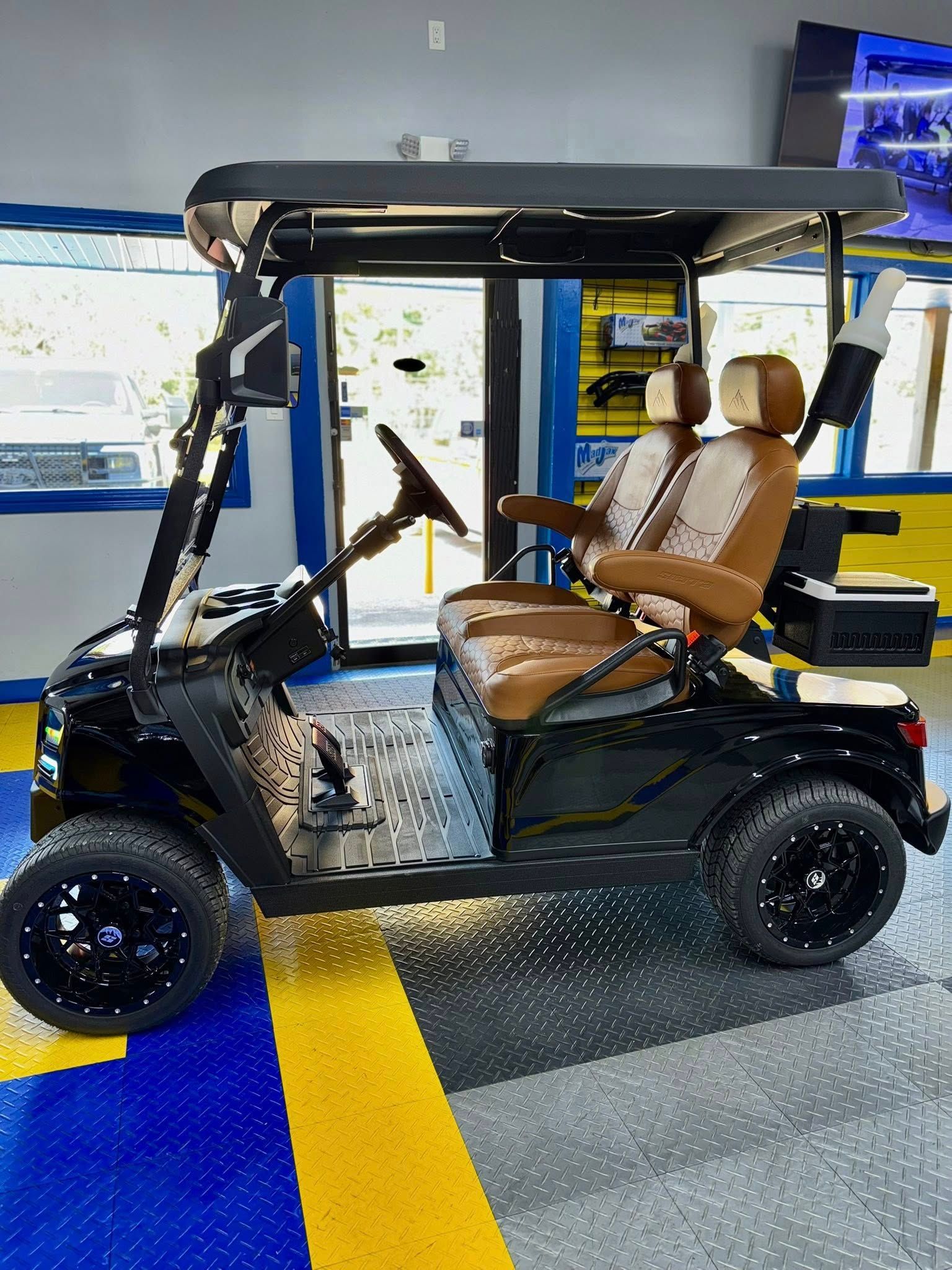 Black golf cart with brown and cream seats, black wheels, parked indoors.
