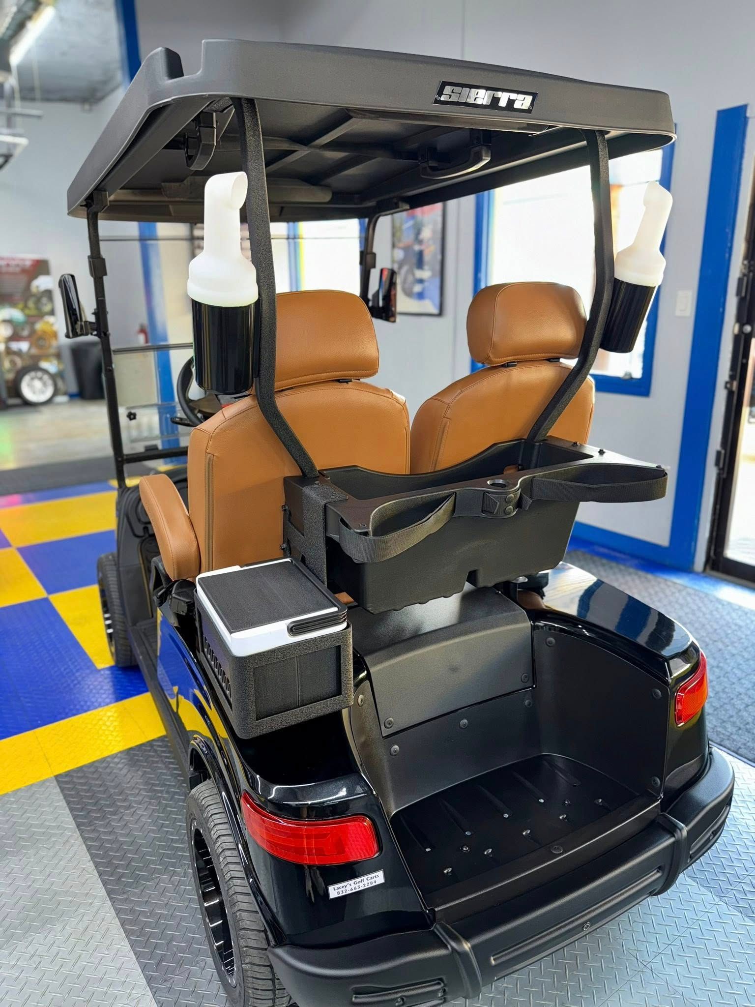 Black golf cart with brown seats, a cooler, and bottles inside a garage.