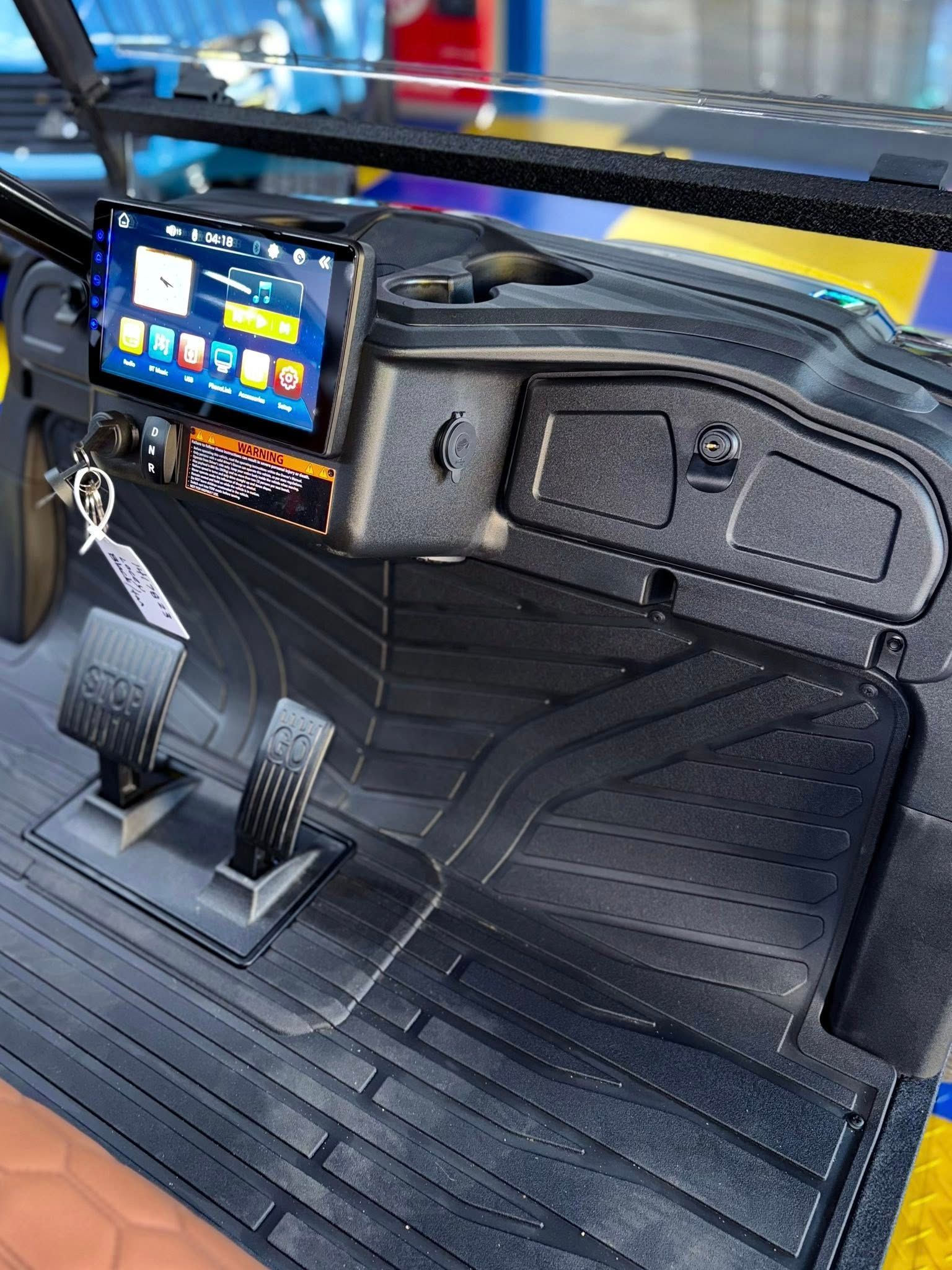 Black golf cart dashboard with touchscreen, pedals, and rubber floor mat.