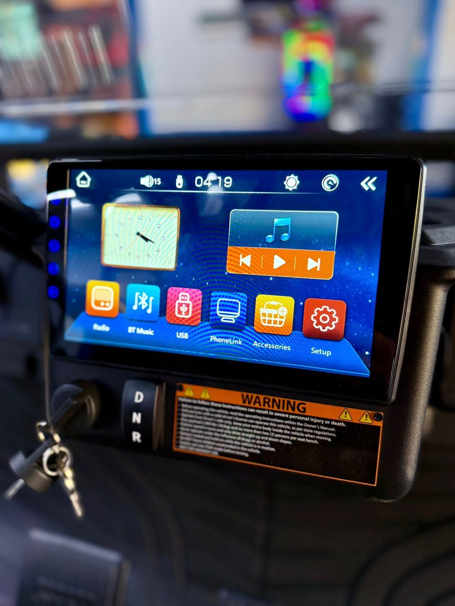 A car radio touchscreen with colorful icons. Dashboard includes gear selection, warning label, and keys.
