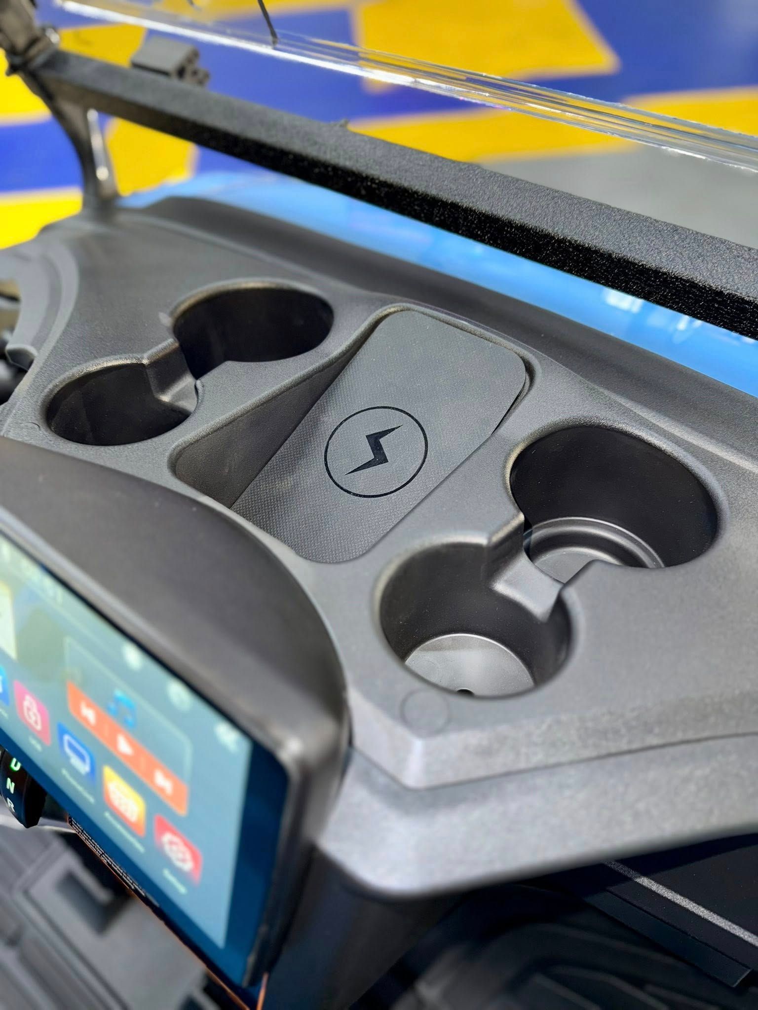 Black golf cart console with cup holders and wireless charging pad.