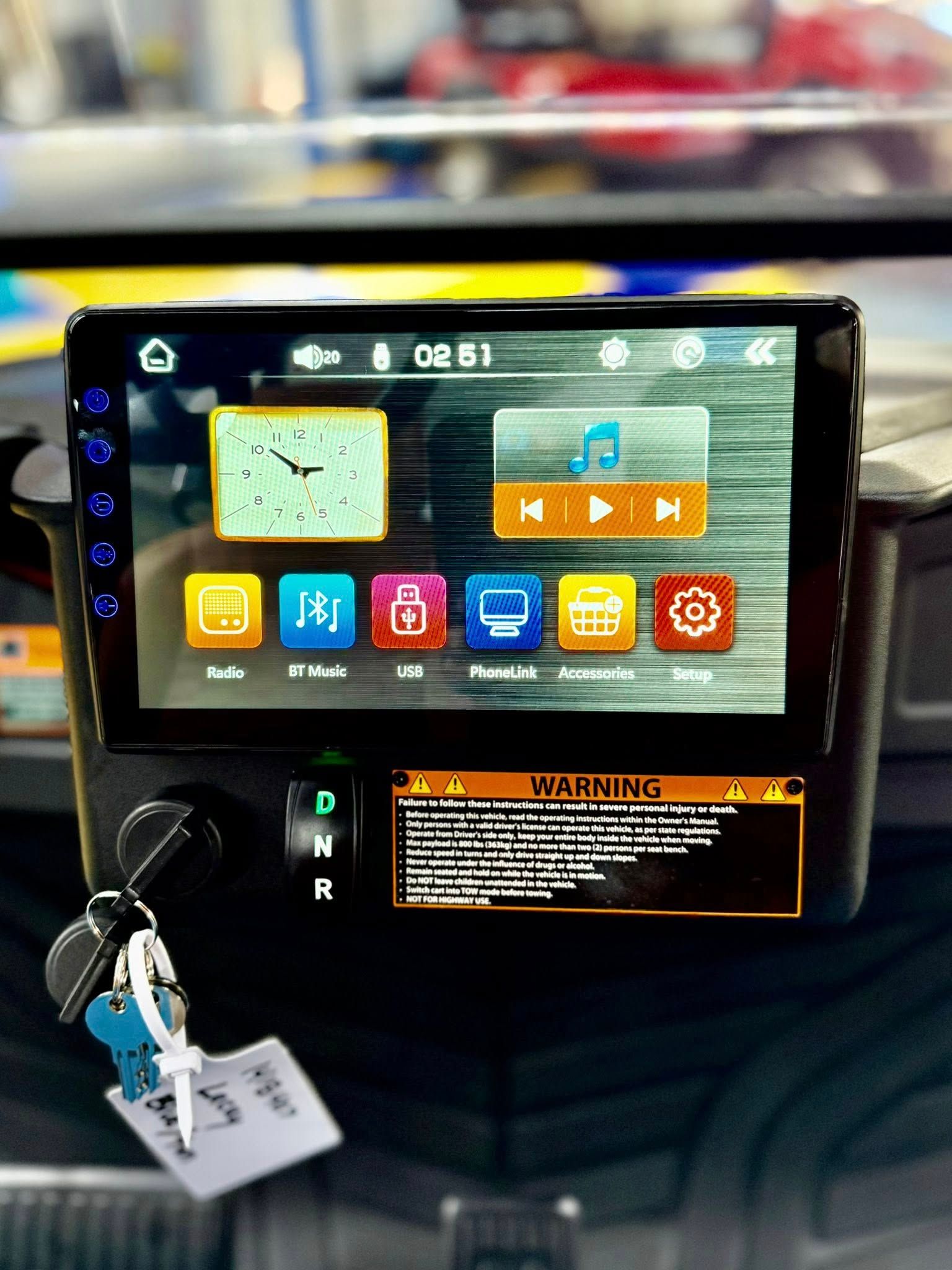 Golf cart dashboard with multimedia screen, key, and warning label.