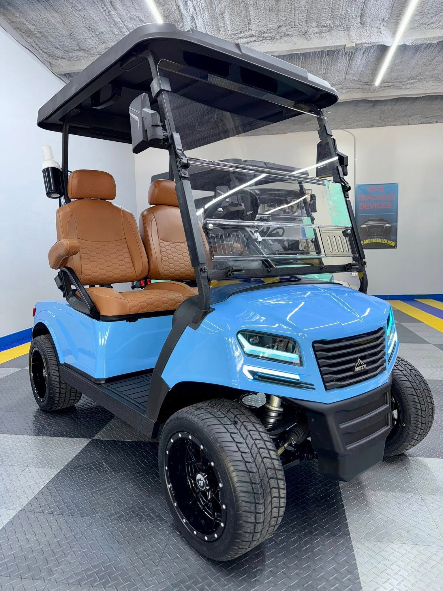 Blue golf cart with brown seats, black roof, and tires, indoors.