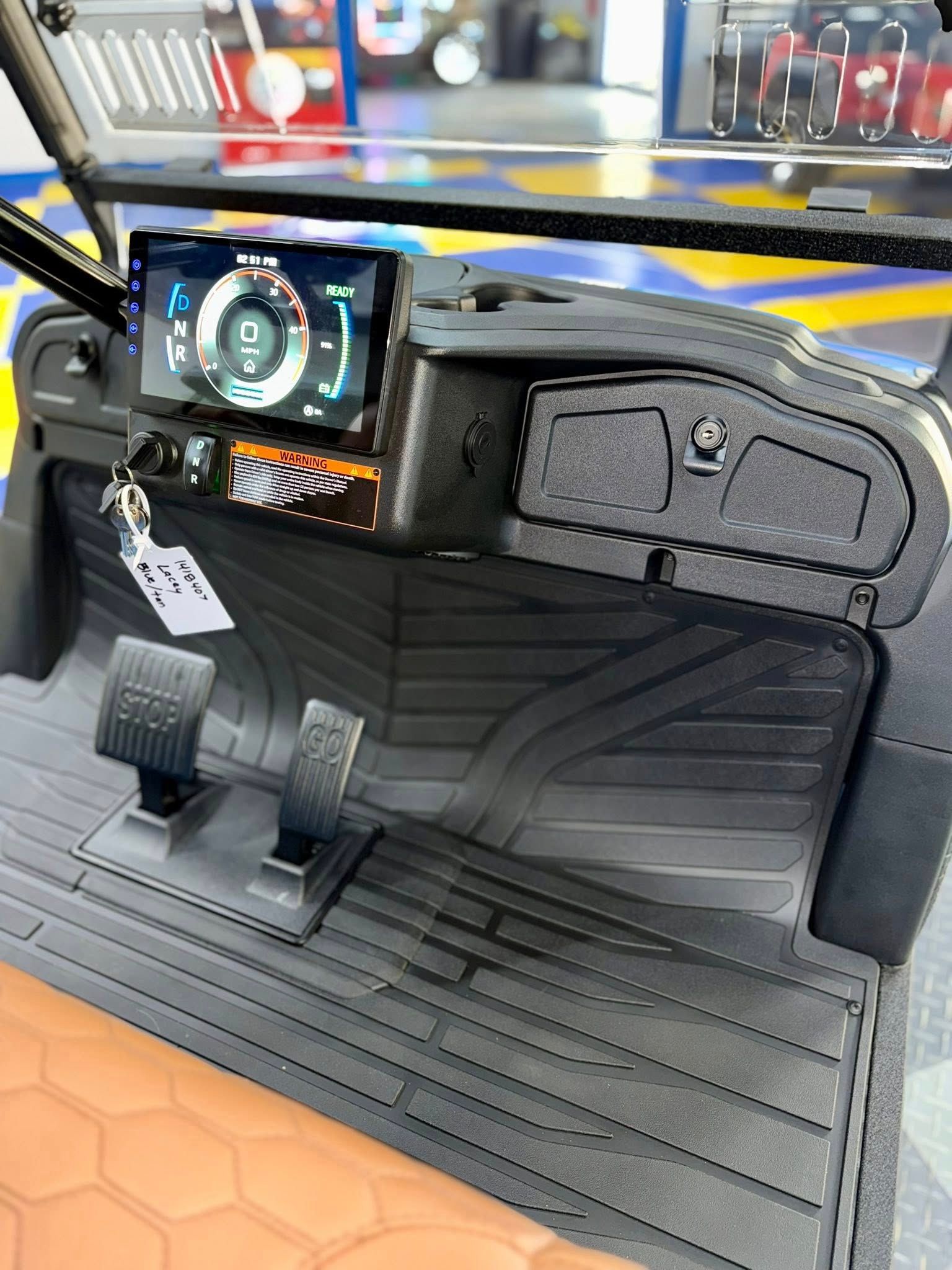 Golf cart dashboard with digital speedometer, pedals, and storage compartment.