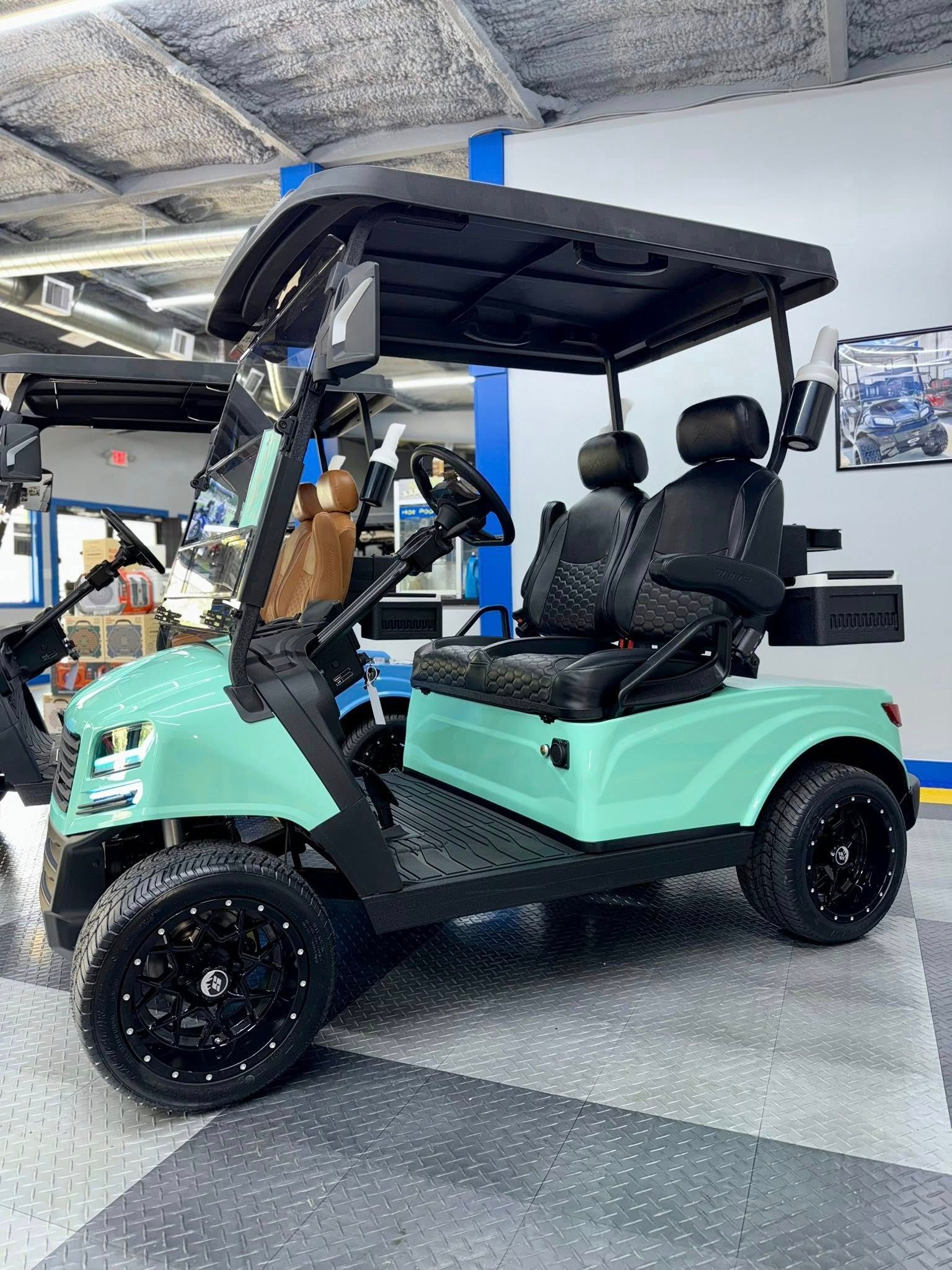Mint green golf cart with black accents, black seats, and black wheels, parked indoors.