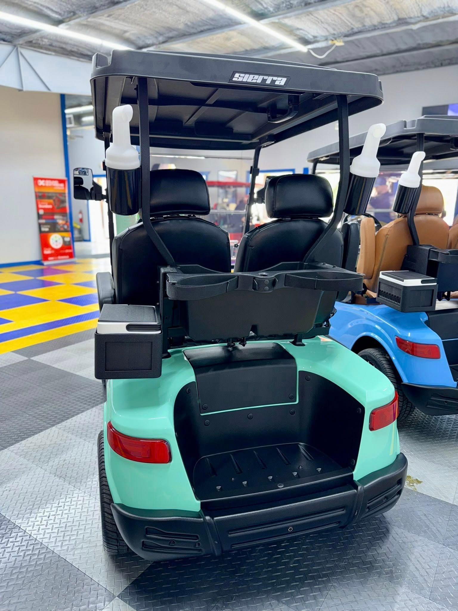 Mint green golf cart with black seats, roof, and rear storage area, indoors.