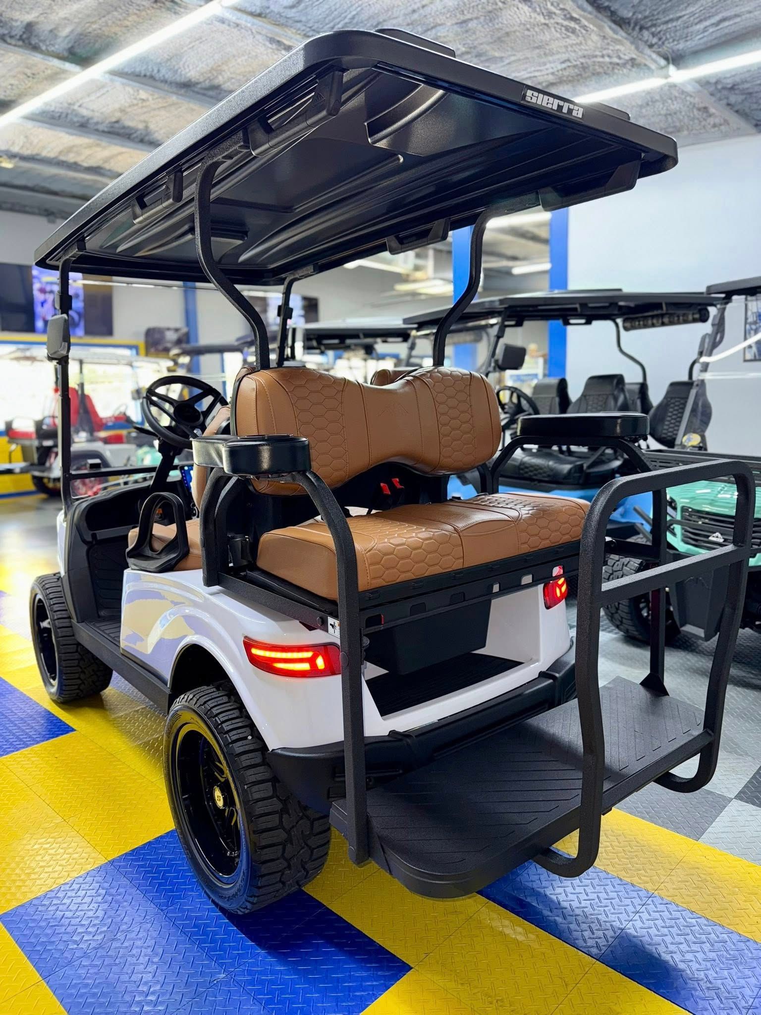 White golf cart with black accents, brown seats, and black off-road tires, parked indoors.