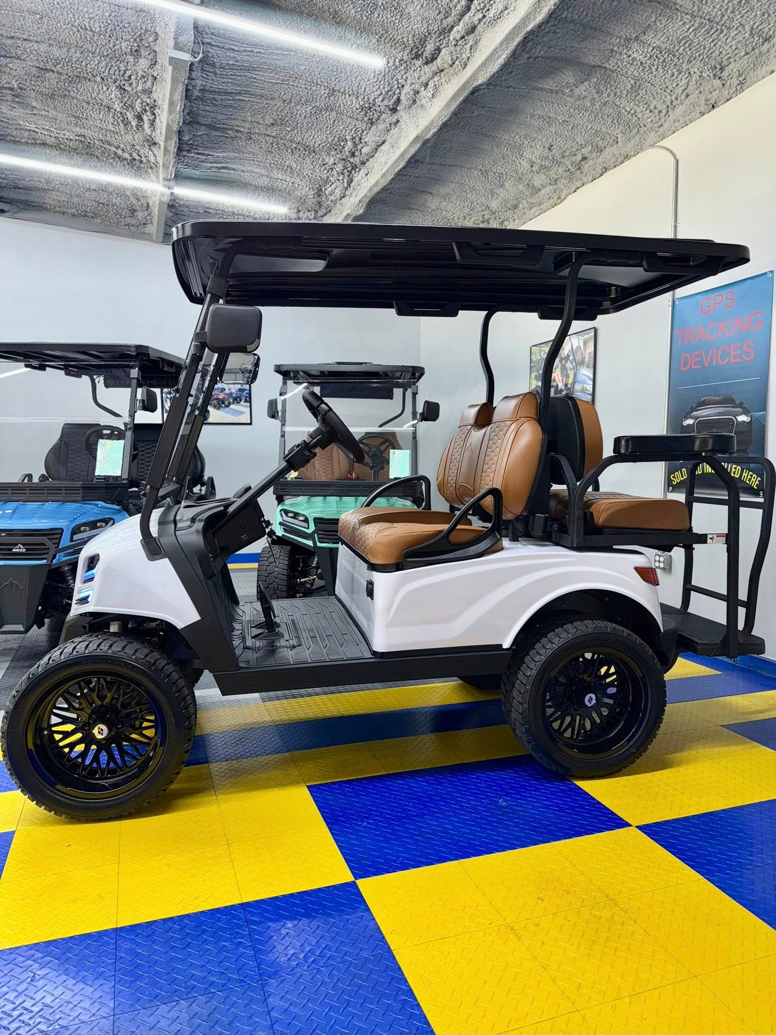 White golf cart with black trim and custom wheels, brown seats, indoors on checkered floor.