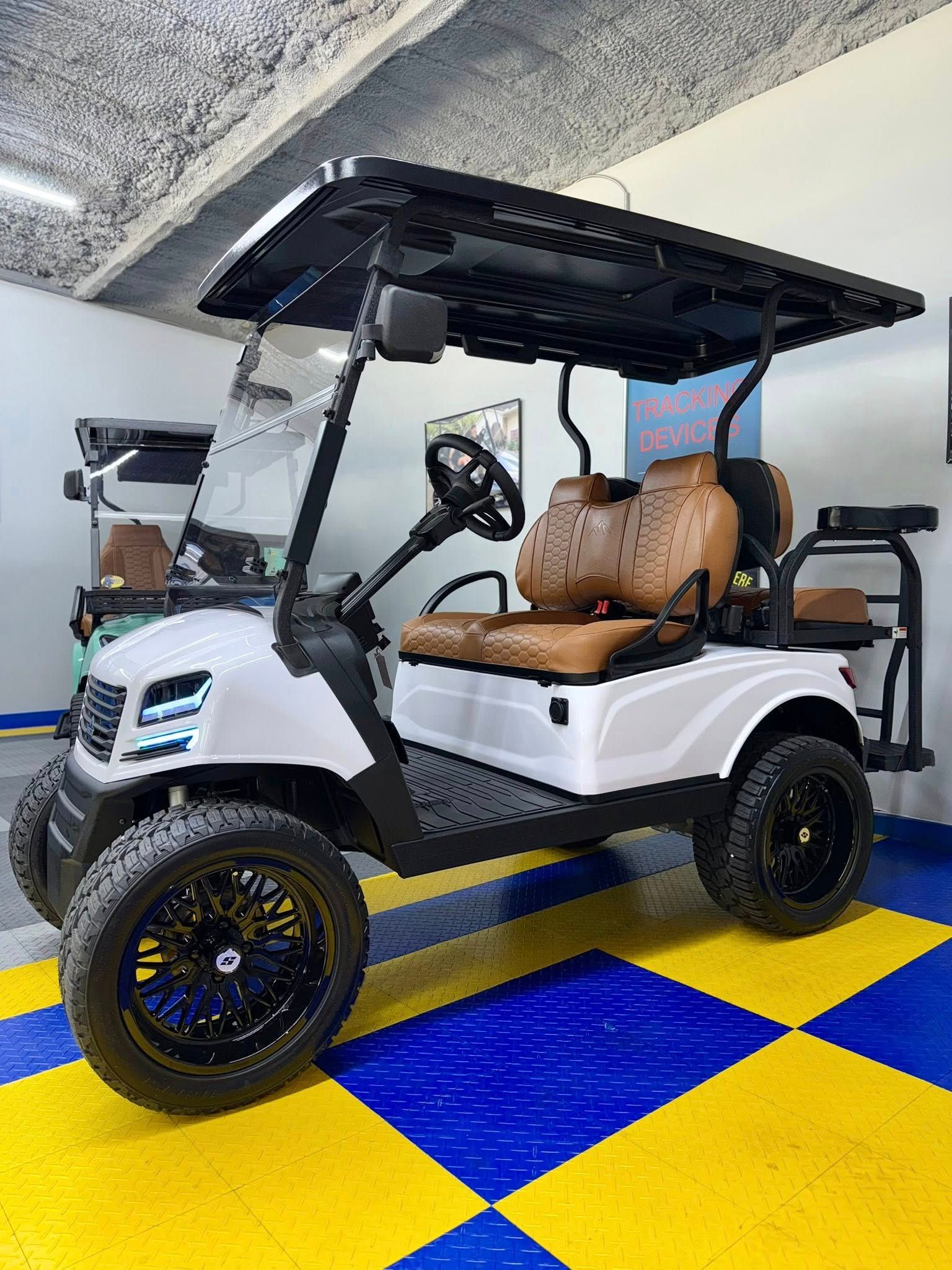 White golf cart with brown seats, black wheels and roof, on a blue and yellow checkered floor.