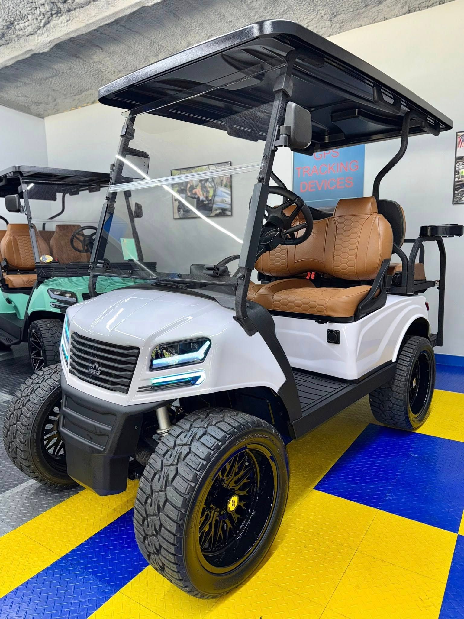 White custom golf cart with black wheels and tan seats, parked indoors.