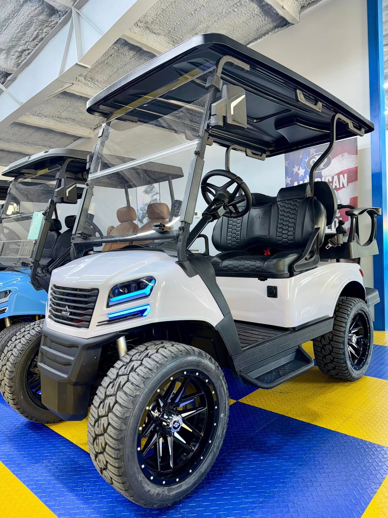 White and black customized golf cart with large tires, parked indoors.