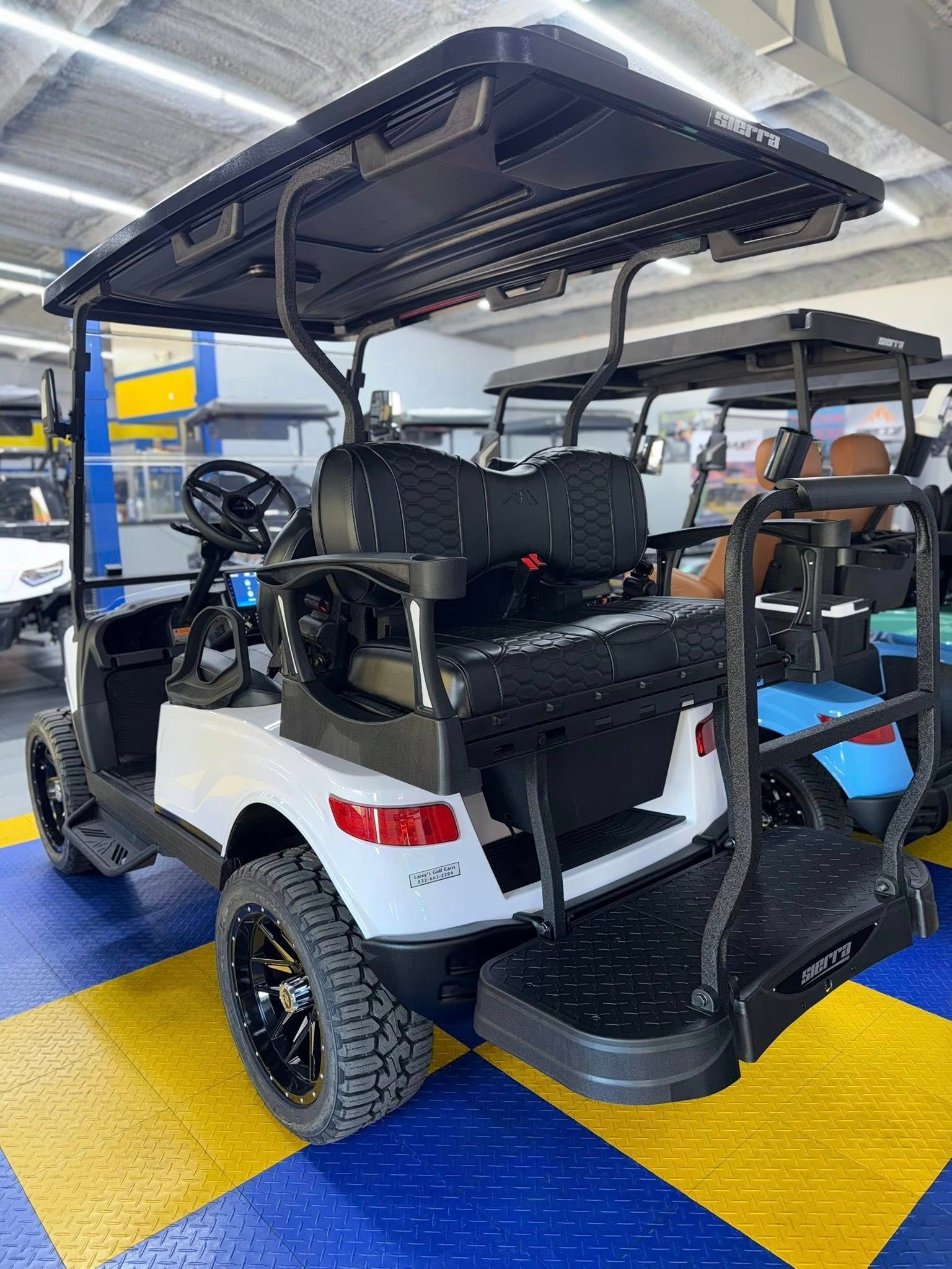 White golf cart with black accents, rear-facing seat, and step platform, parked indoors.