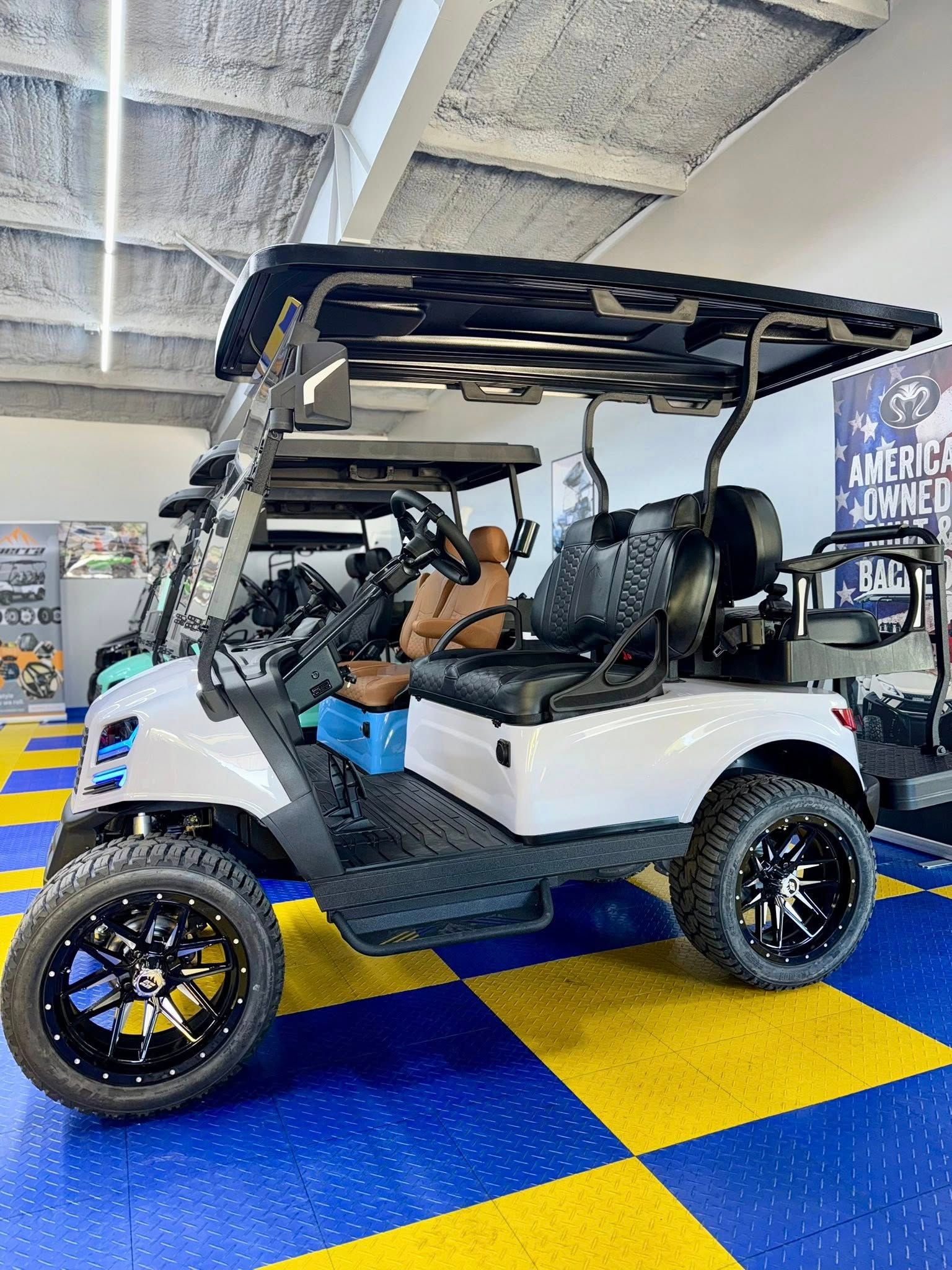 White golf cart with black accents, custom wheels, and canopy parked on blue and yellow checkered floor.