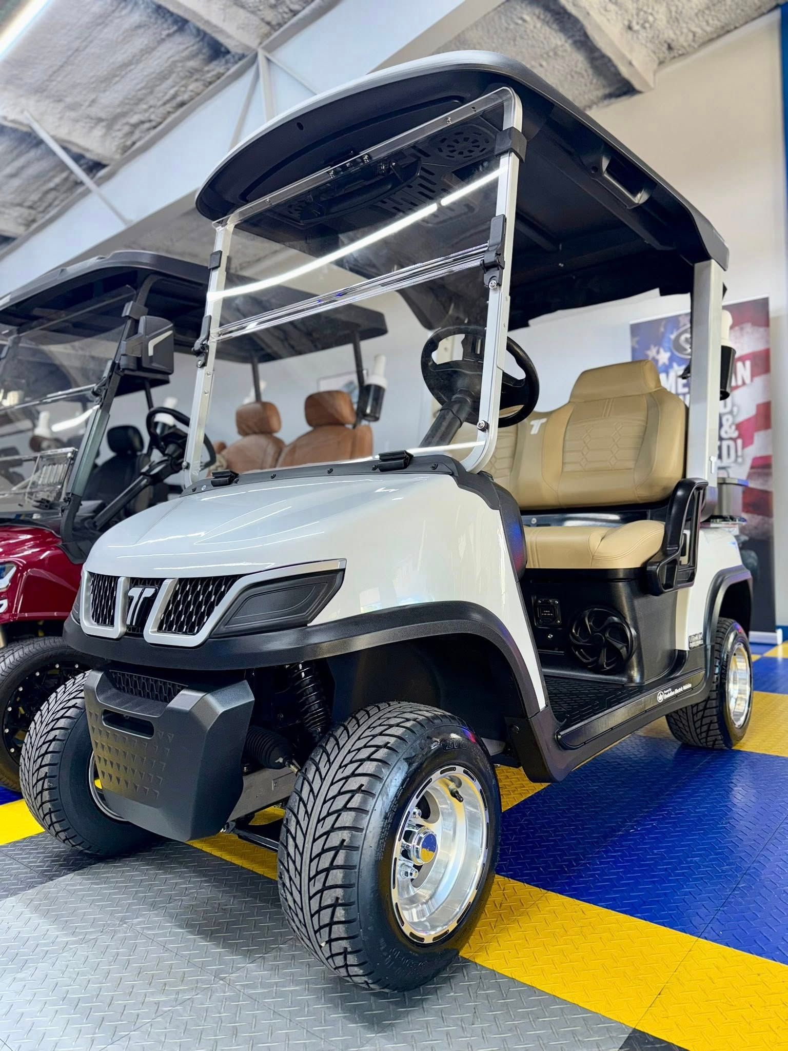 White and black golf cart with tan seats parked indoors on a blue and yellow floor.