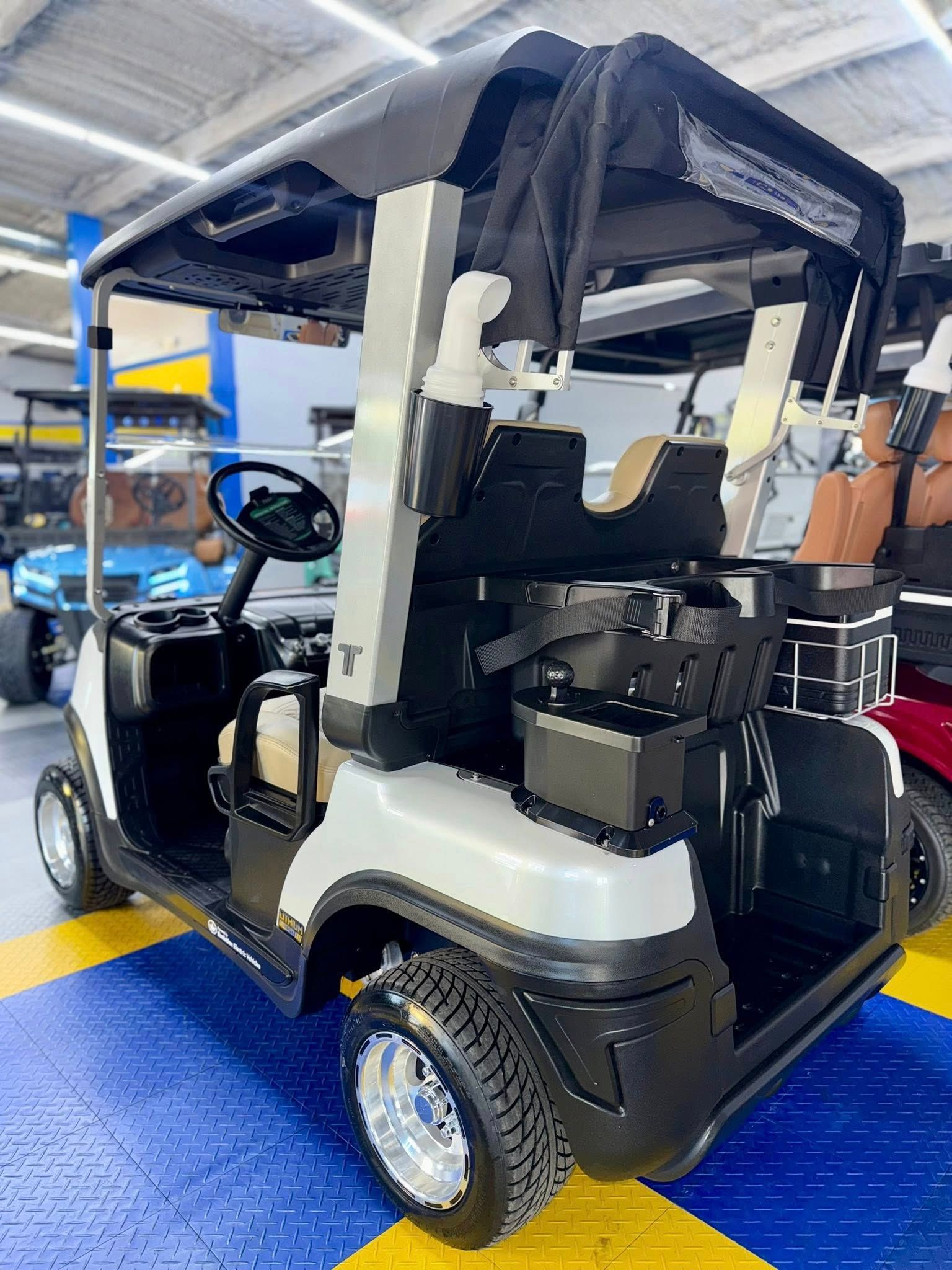 White and black golf cart with black canopy, parked indoors on a blue, yellow, and black tiled floor.