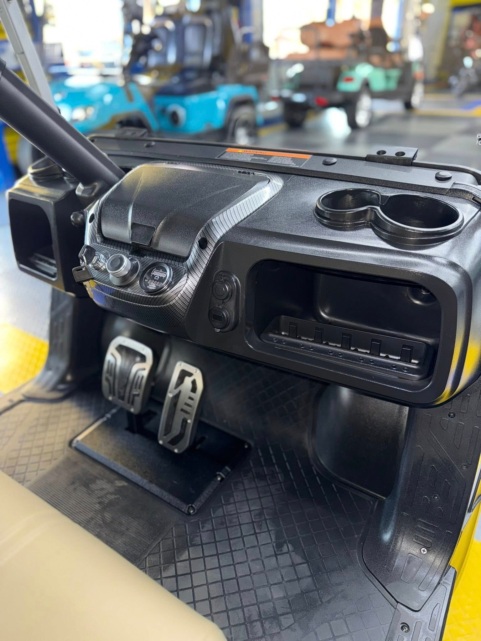 Dashboard of a black golf cart with cup holders, pedals, and lights.