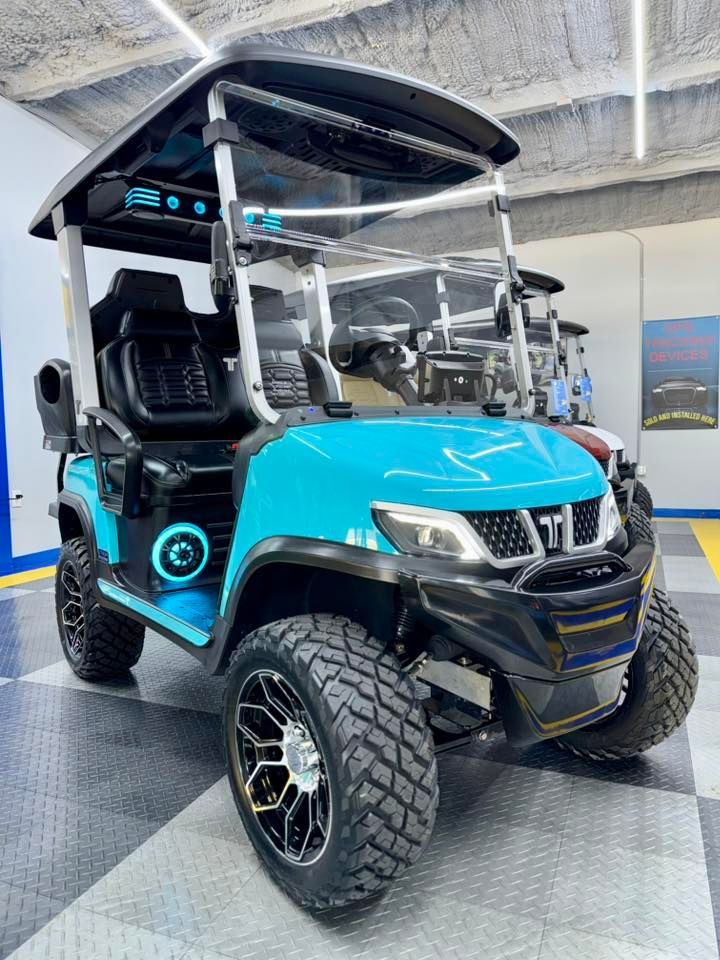Aqua golf cart with black accents, rugged tires, in a garage setting.