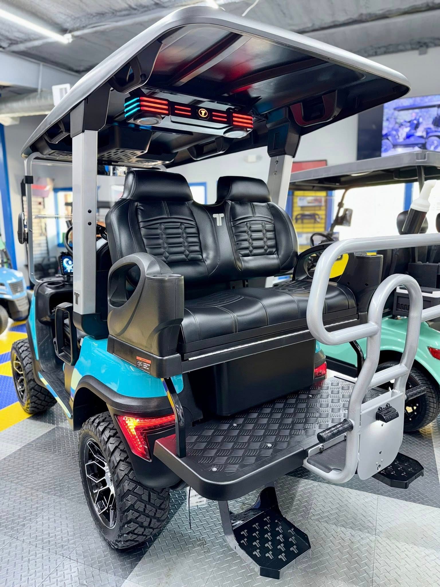 Teal golf cart with black seats, large wheels, and a rear step.