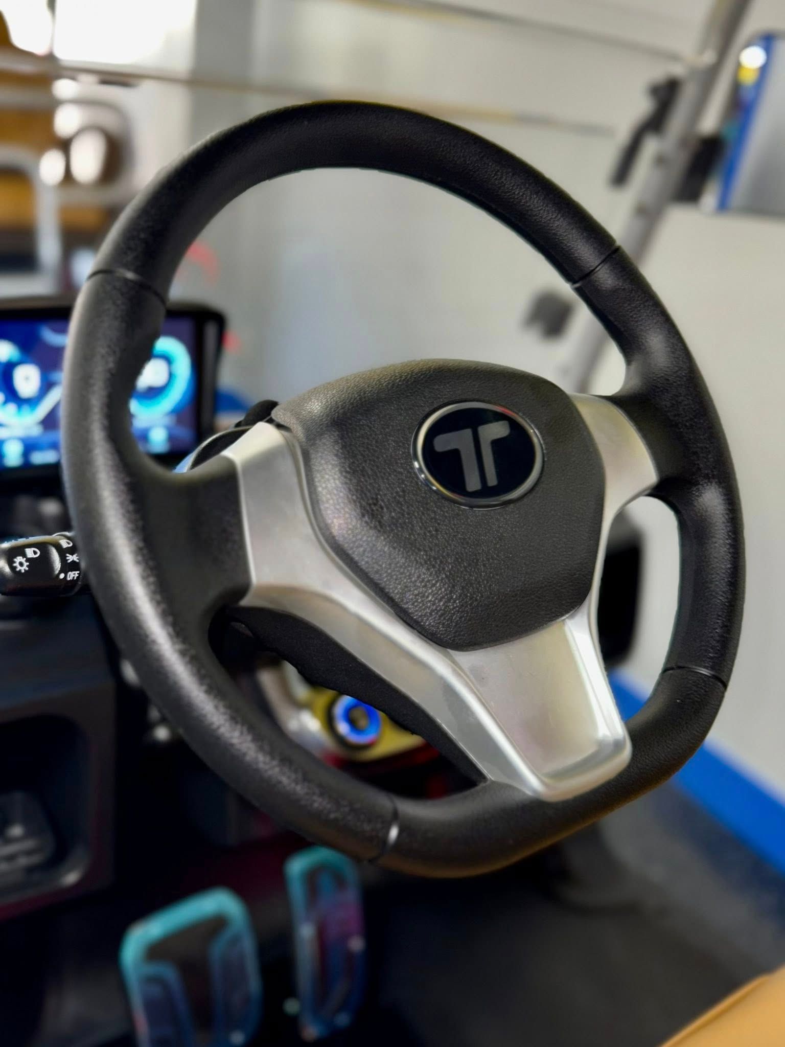 Black steering wheel with a silver hub and a blue-lit display in the background. A golf cart's interior is visible.
