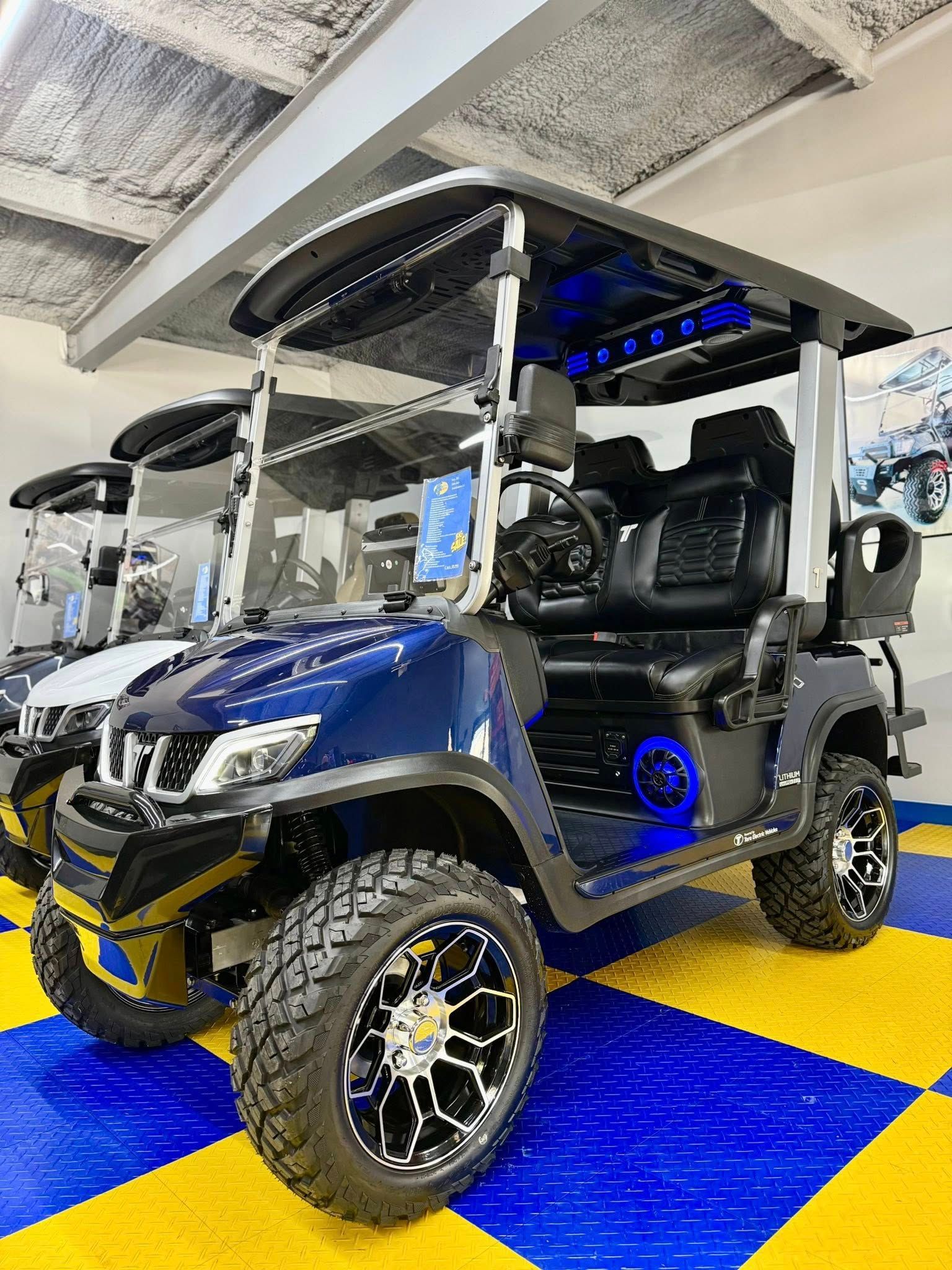 A custom navy blue golf cart with black accents, a lifted suspension, and large black and chrome wheels parked indoors on a tiled floor.