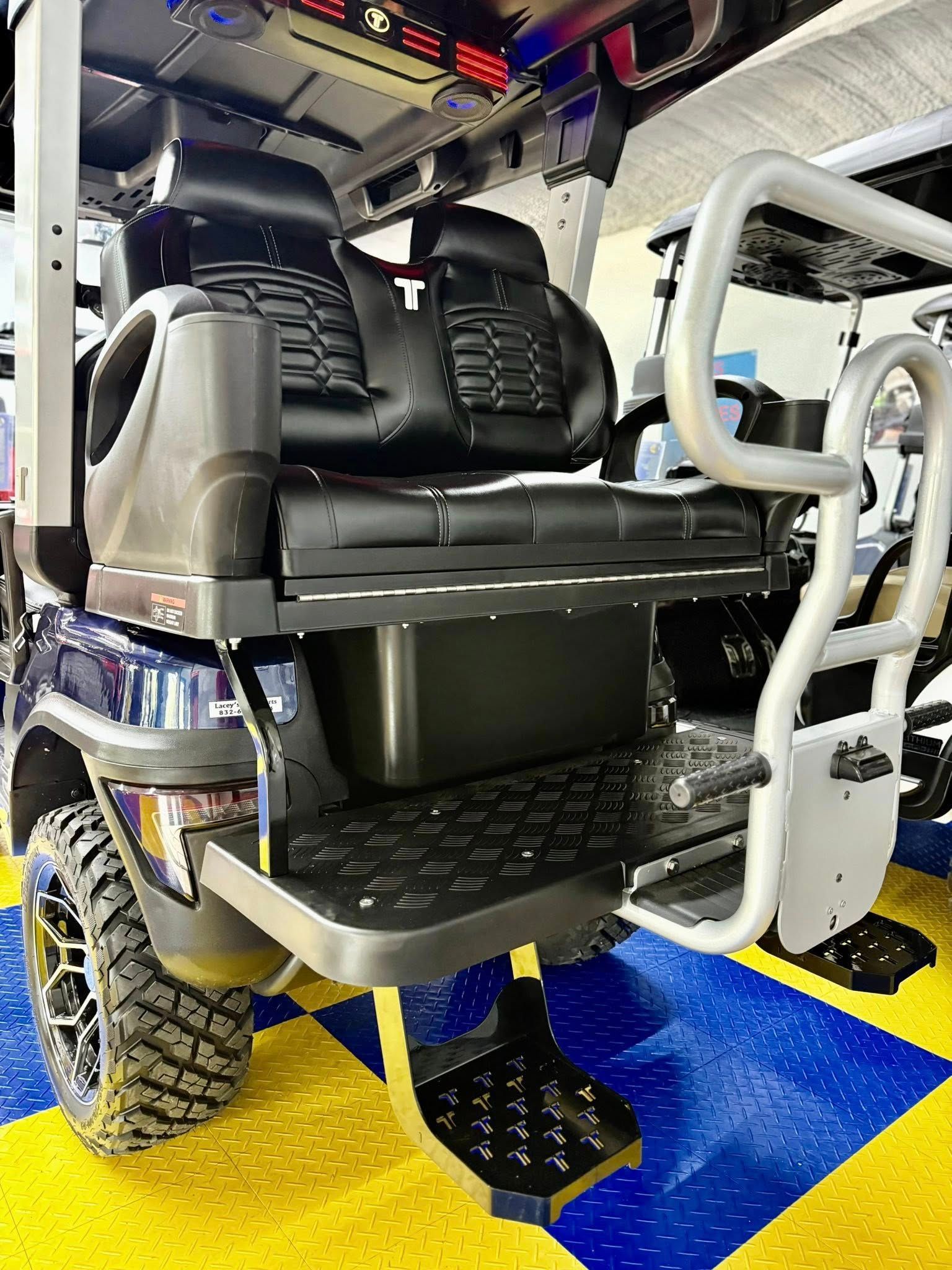 A custom golf cart with black seating and a rear step platform. The cart is on a blue and yellow floor.