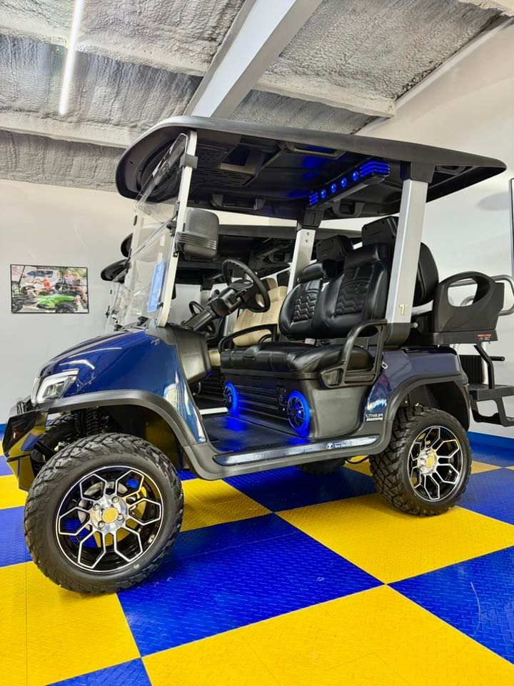Blue and black customized golf cart with aftermarket wheels and LED lighting, parked on a blue and yellow checkered floor.