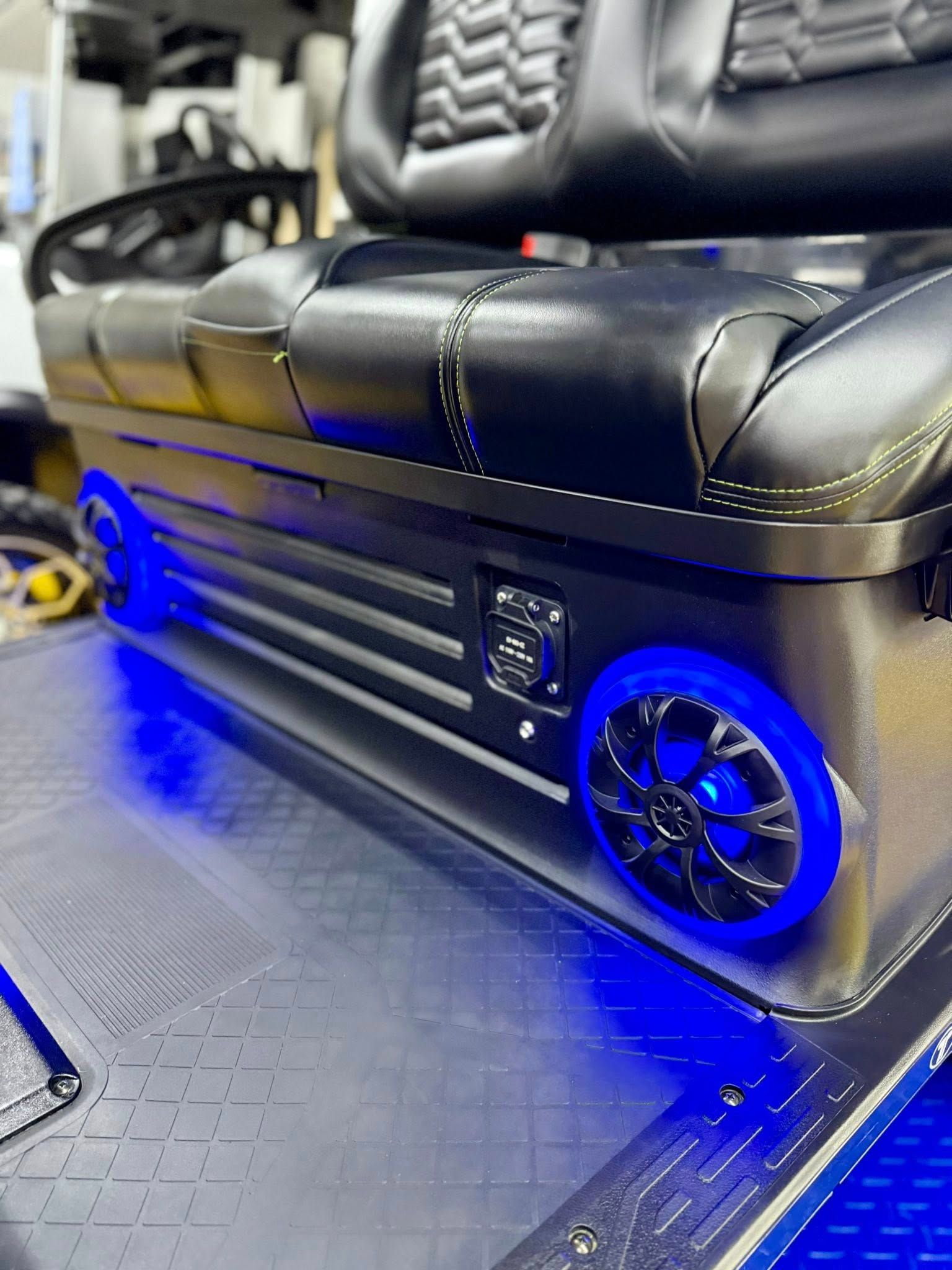 Black and silver golf cart seat with blue LED lights around speakers. Leather upholstery and storage compartment.