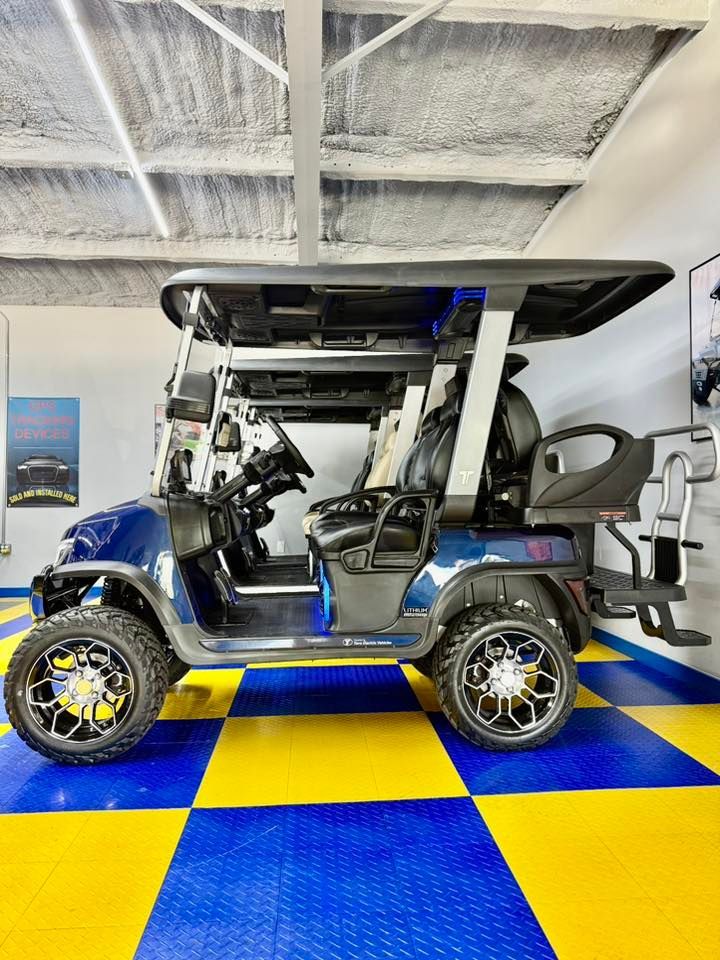 A blue golf cart with black wheels and a canopy sits indoors on a blue and yellow checkered floor.