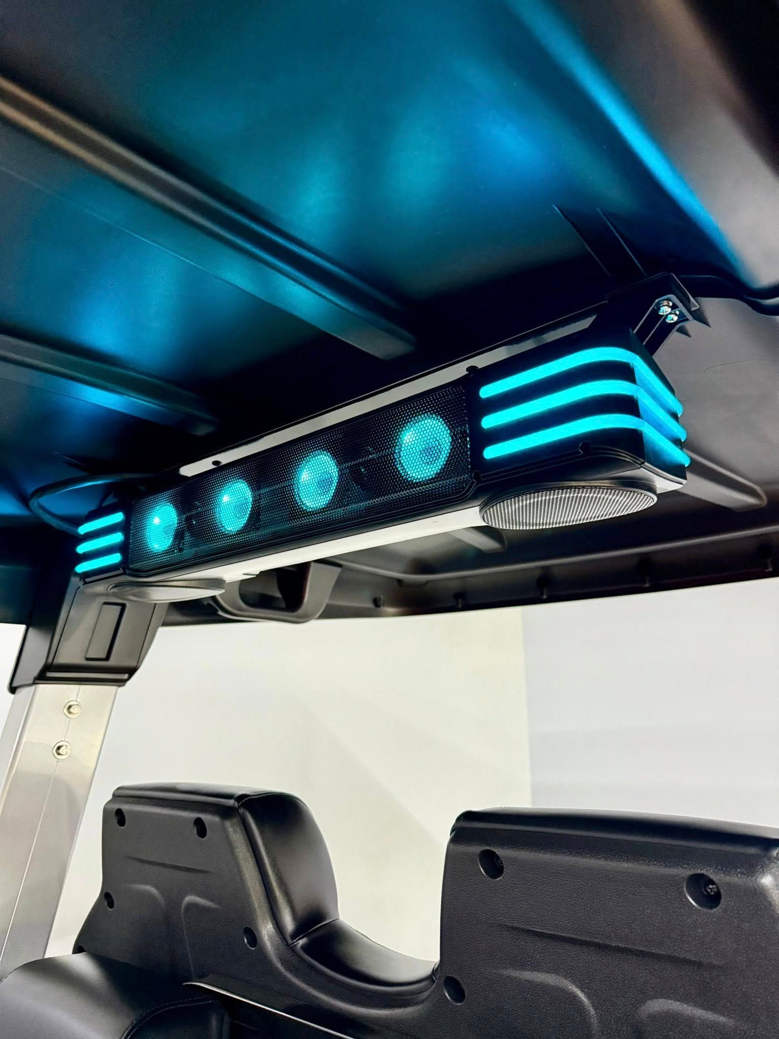 Blue LED speaker system mounted on the roof of a golf cart, illuminating the interior.