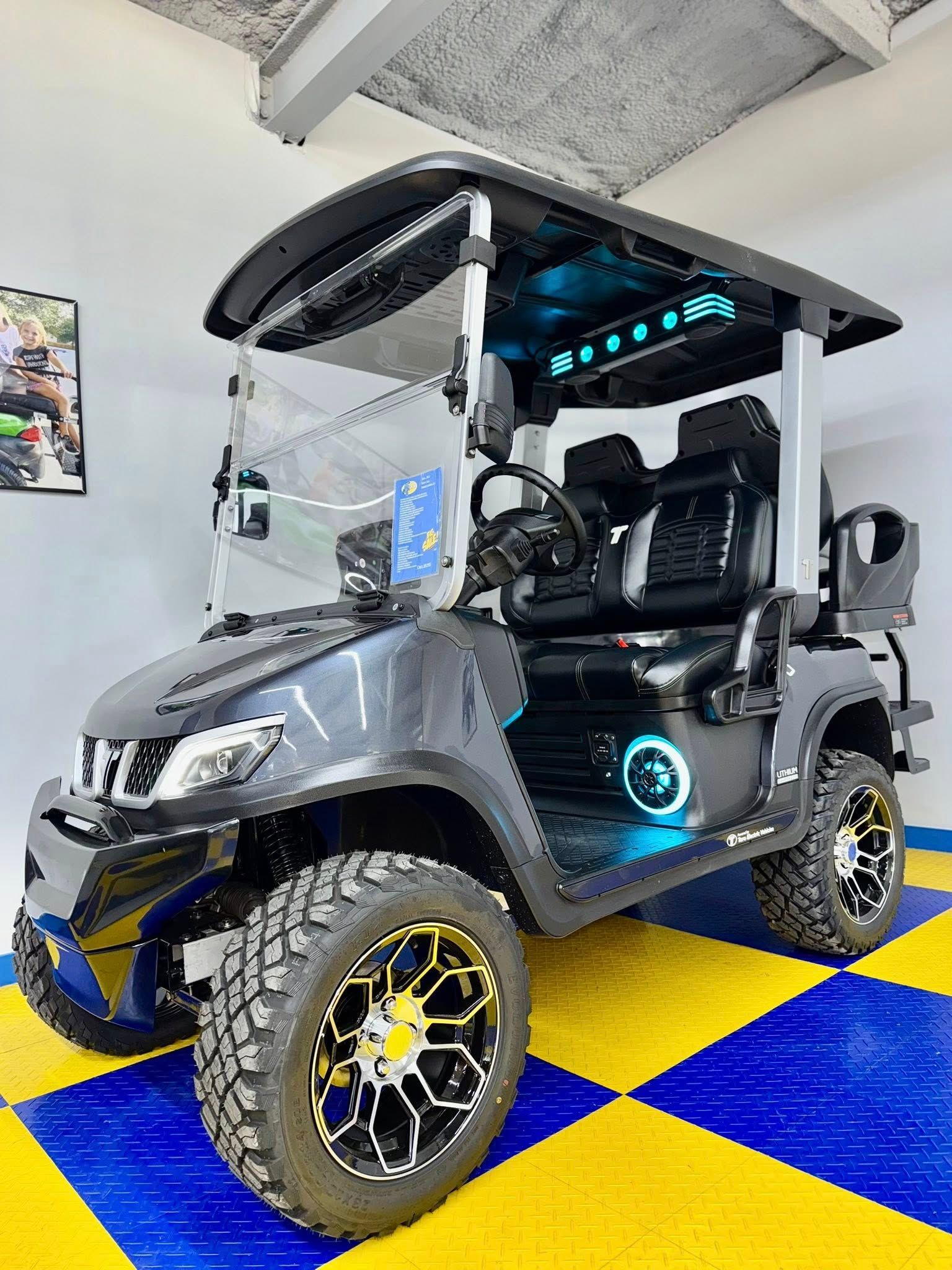 Dark gray golf cart with black accents, off-road tires, and LED lighting on display in a showroom with checkered flooring.