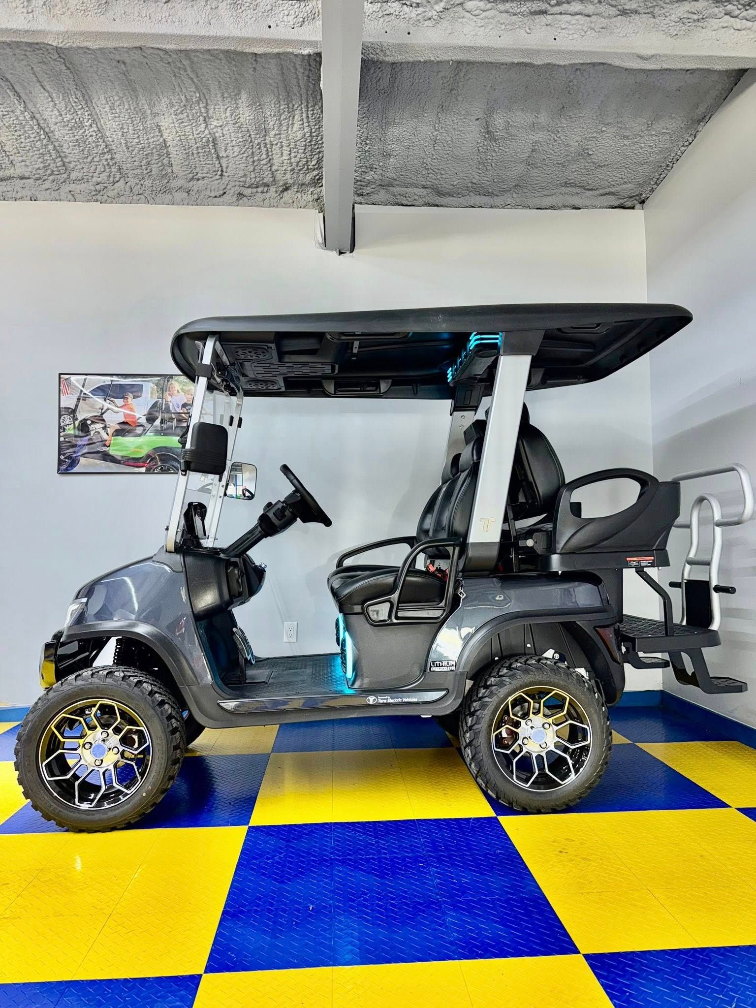 Gray golf cart with black roof and custom wheels on a yellow and blue checkered floor.