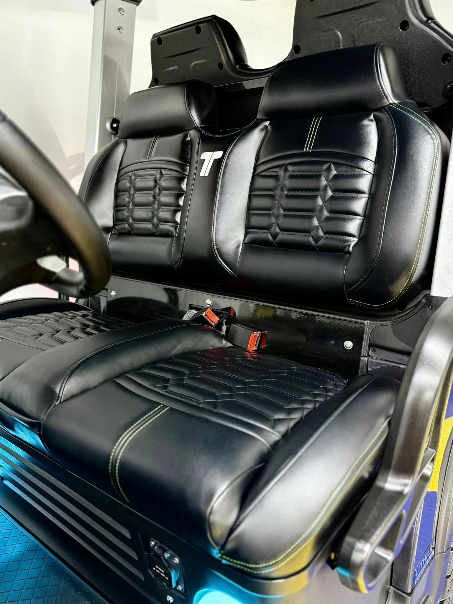 Black leather golf cart seats with decorative stitching, steering wheel visible. The cart has a modern design.